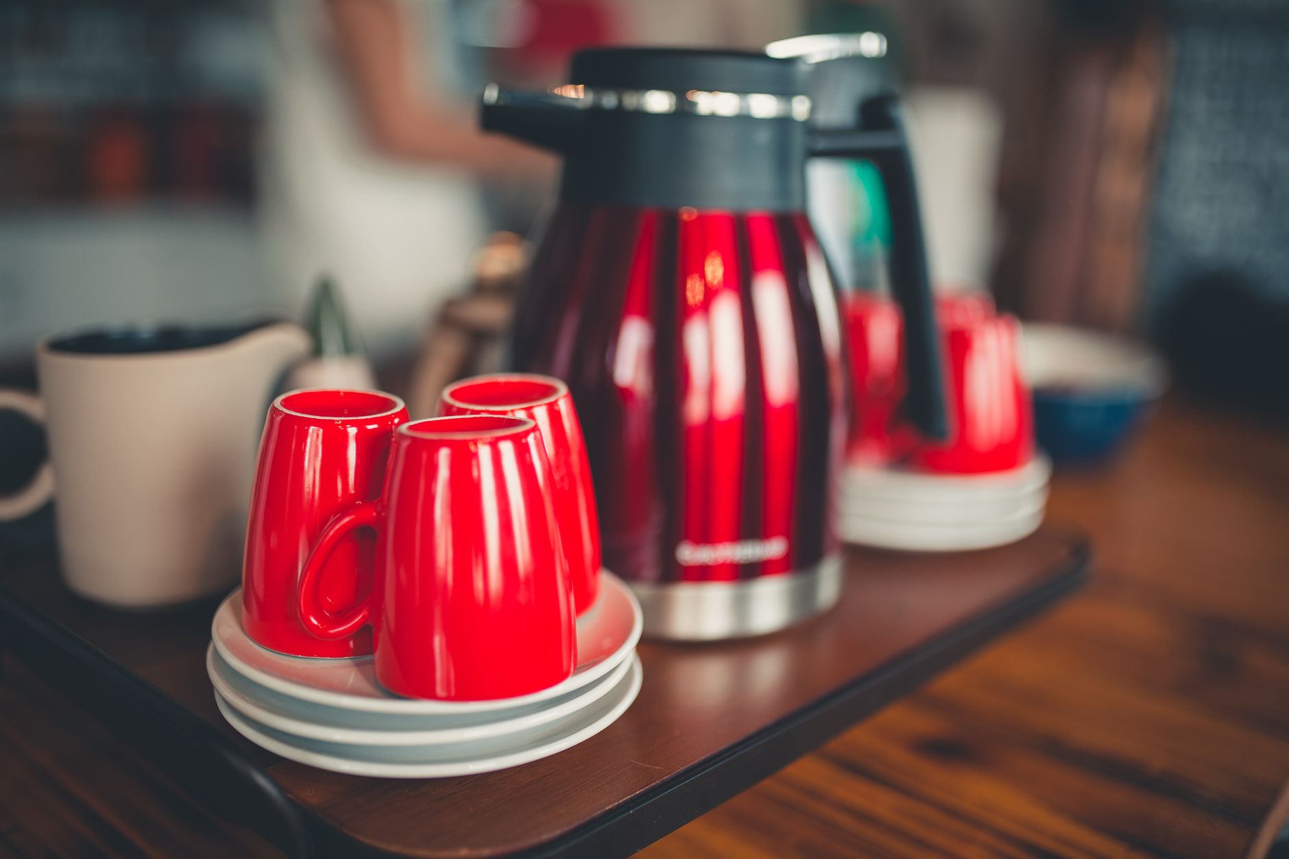 Red ceramic cups paired with a matching kettle on a wooden table, creating a warm kitchen atmosphere.