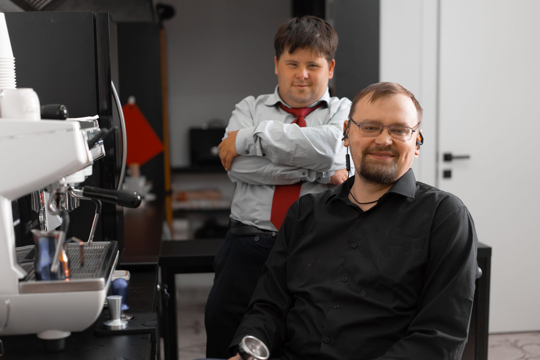 Two coworkers in an office kitchenette enjoying a moment by the coffee machine.