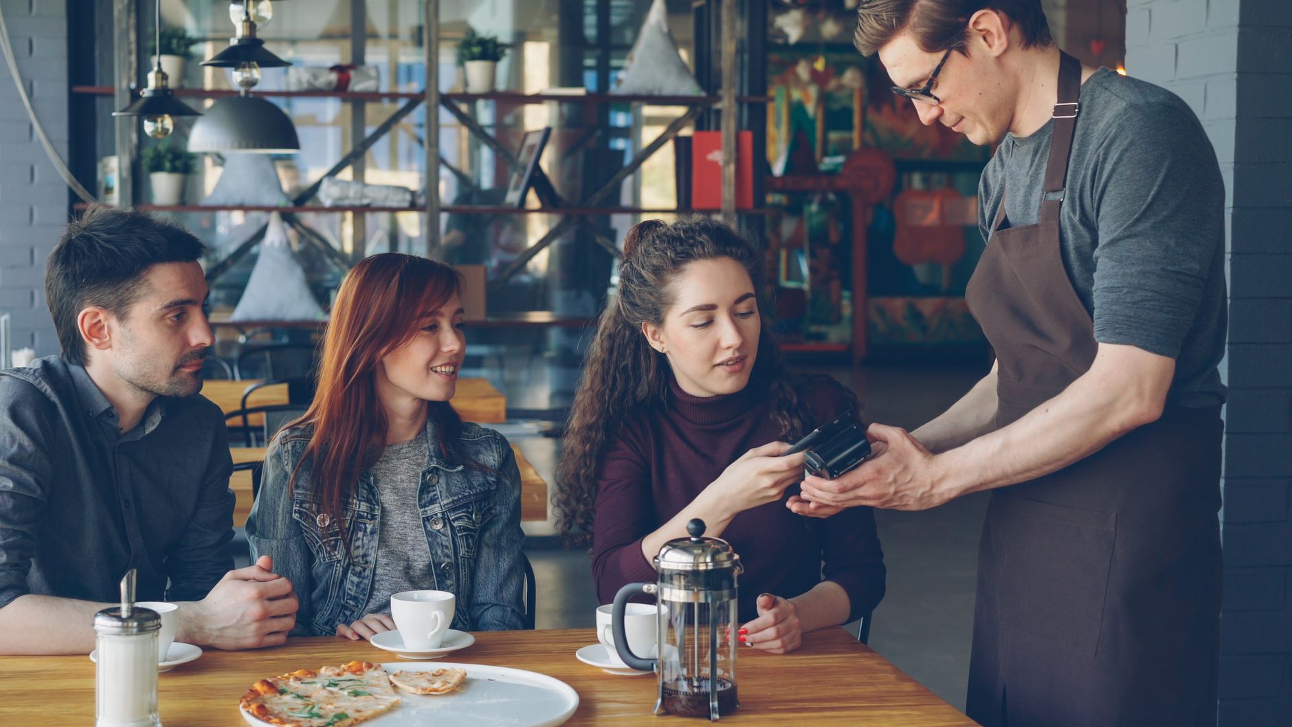 Group of friends having coffee and paying with card in a cozy café setting.