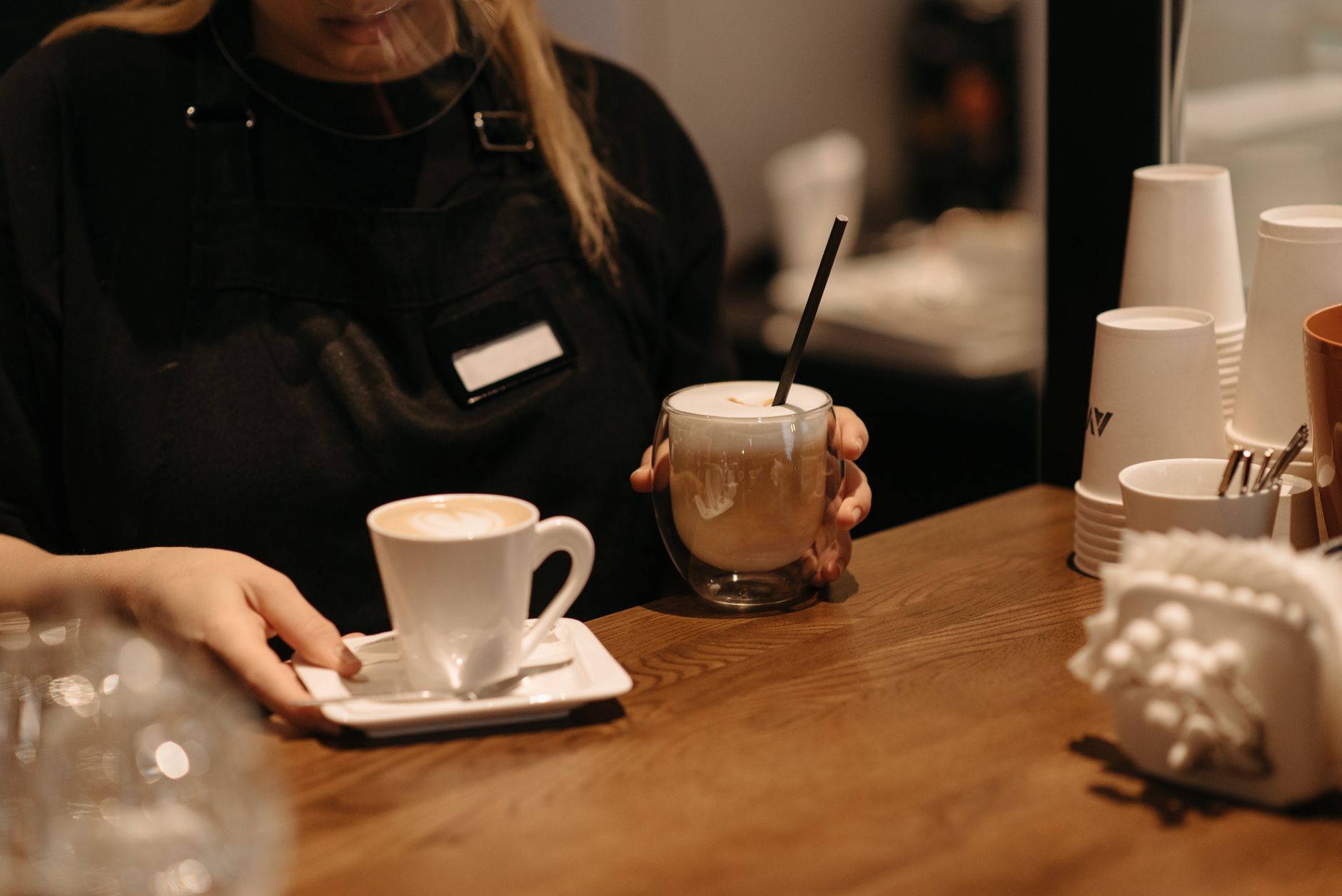 A barista serves coffee drinks in a cozy café atmosphere with a wooden table.