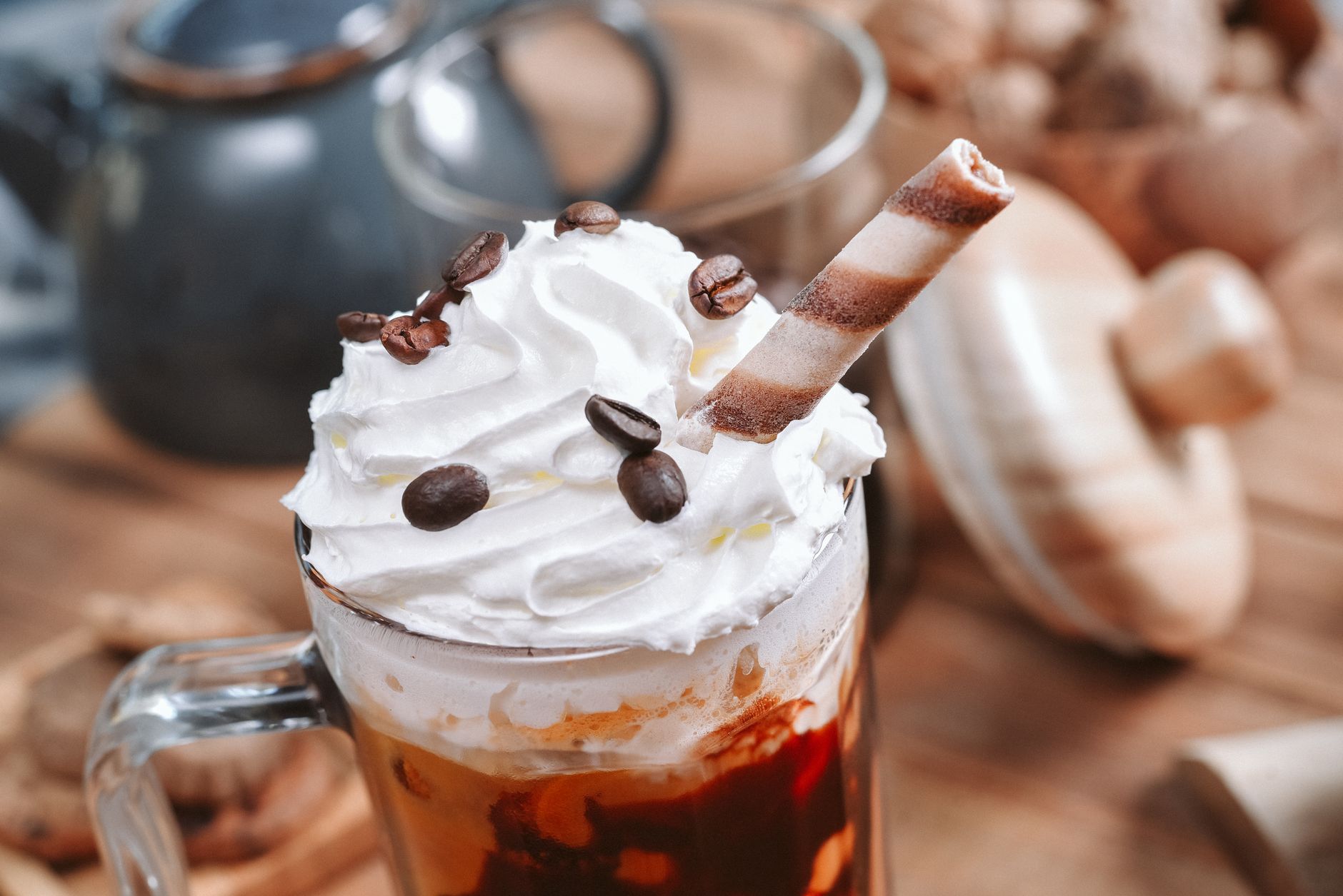 Close-up of a creamy coffee topped with whipped cream, chocolate flakes, and coffee beans.