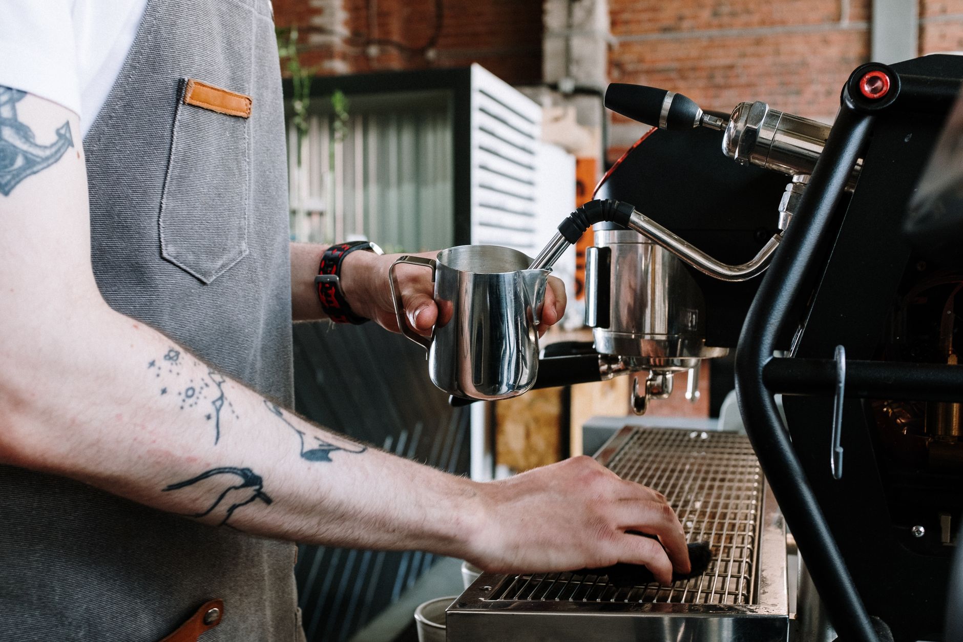 A barista steaming milk for a coffee using an espresso machine, highlighting professional skills in a café environment.