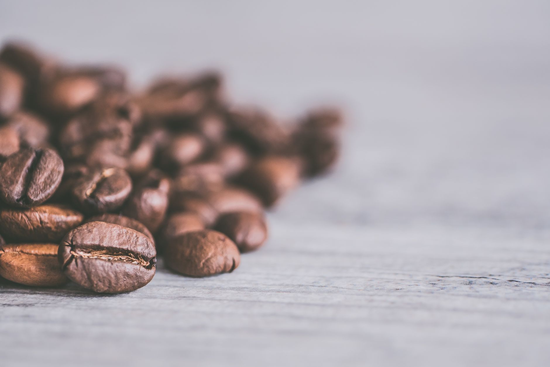 A detailed close-up of aromatic coffee beans scattered on a light wooden surface.