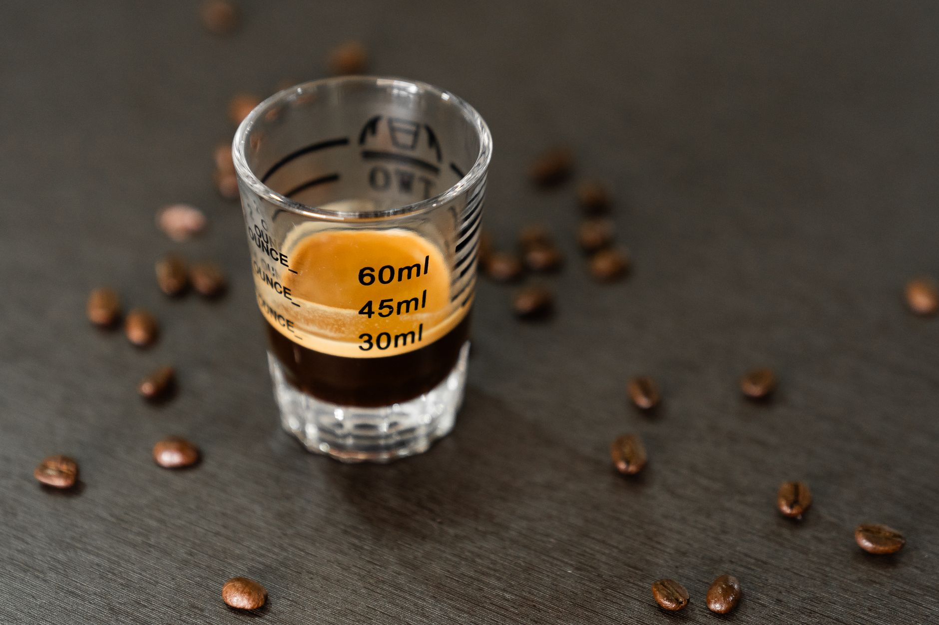 Espresso shot in a measuring glass surrounded by coffee beans, captured in a minimalist style.
