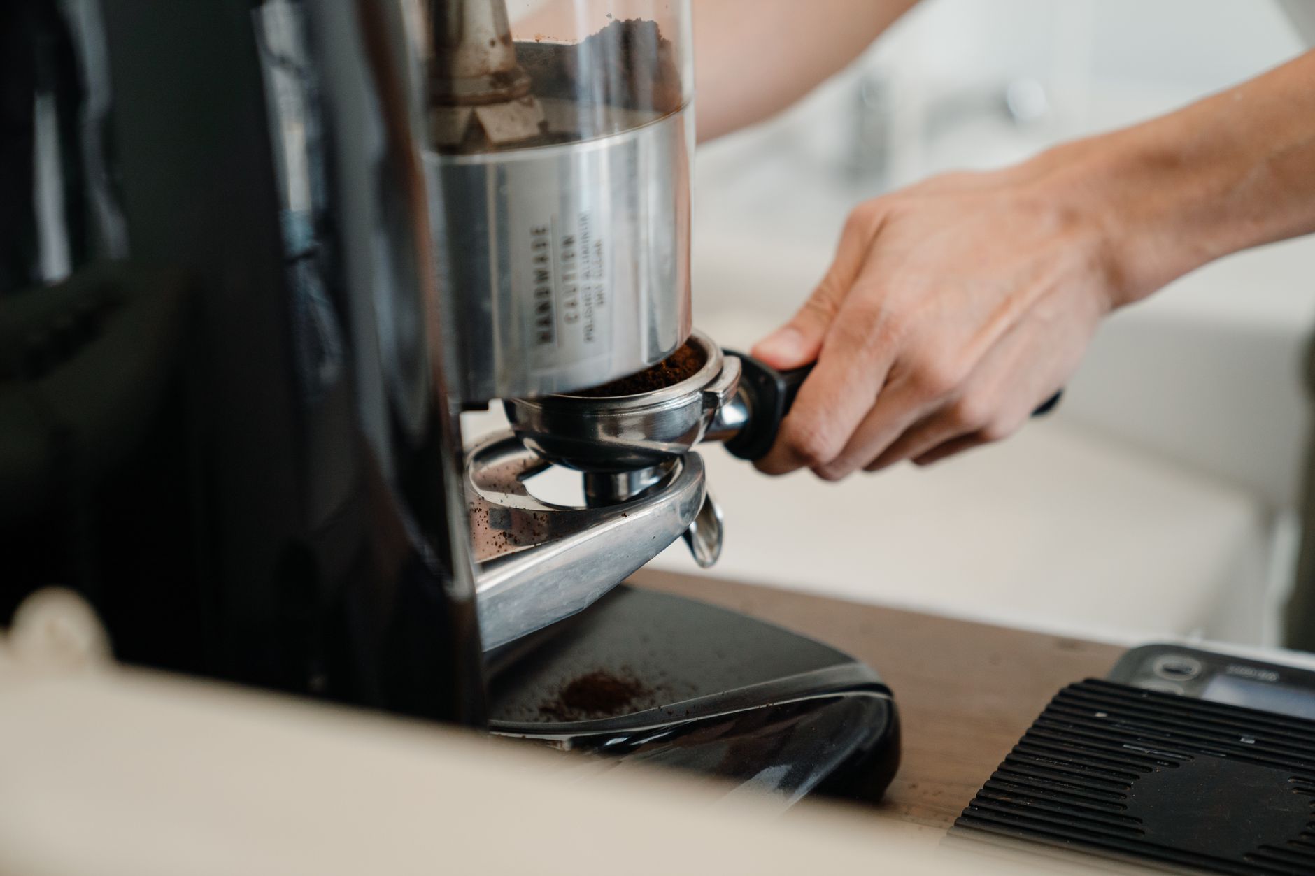 Crop unrecognizable barista grinding freshly roasted coffee beans using modern coffee machine in cafe