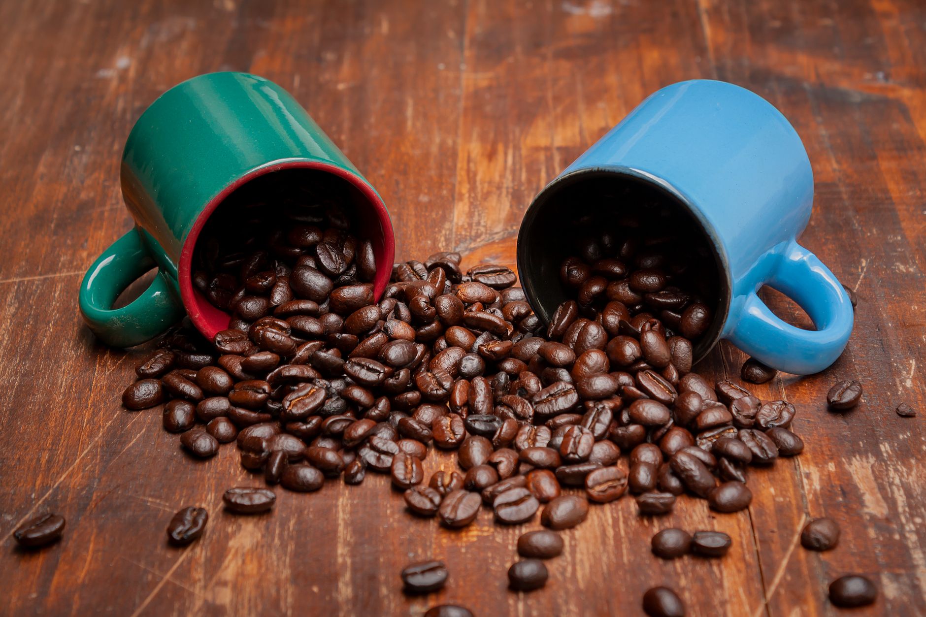 Two mugs spilling coffee beans on a wooden surface, creating a cozy vibe.