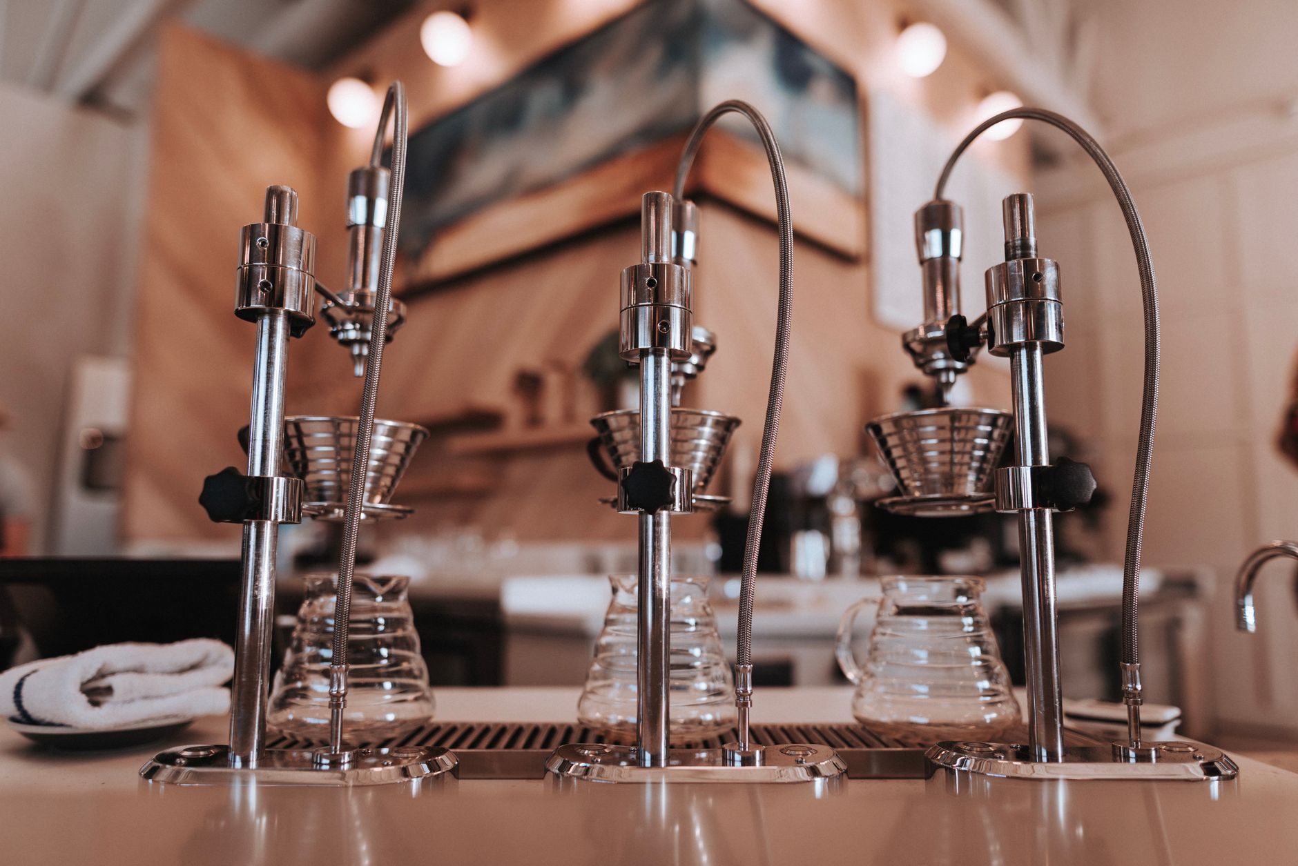 Stainless steel similar drip coffee machine with ribbed filters and transparent glass carafes on table near towel in apartment with artificial light
