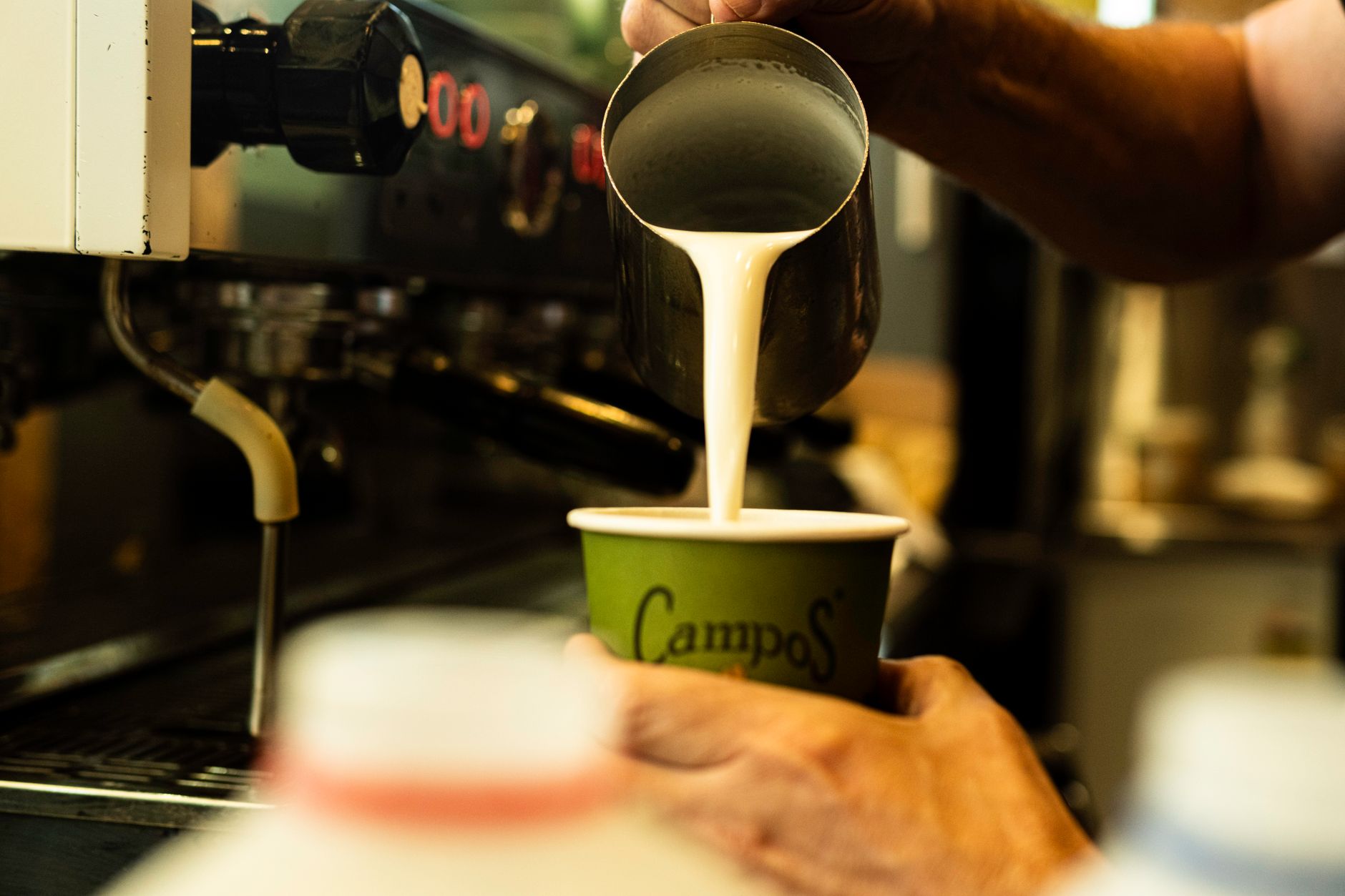 Close-up of a barista preparing a latte with frothed milk at a café.