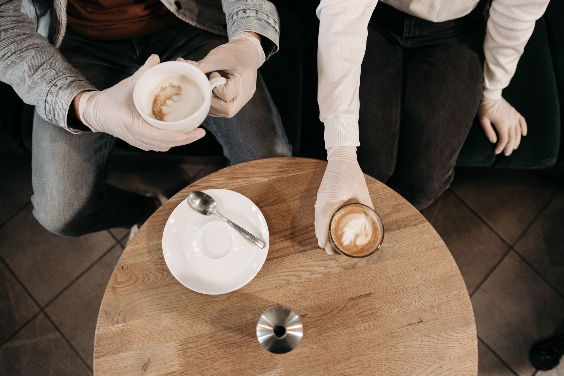Bird's-eye view of barista serving cappuccinos with gloves during the day.
