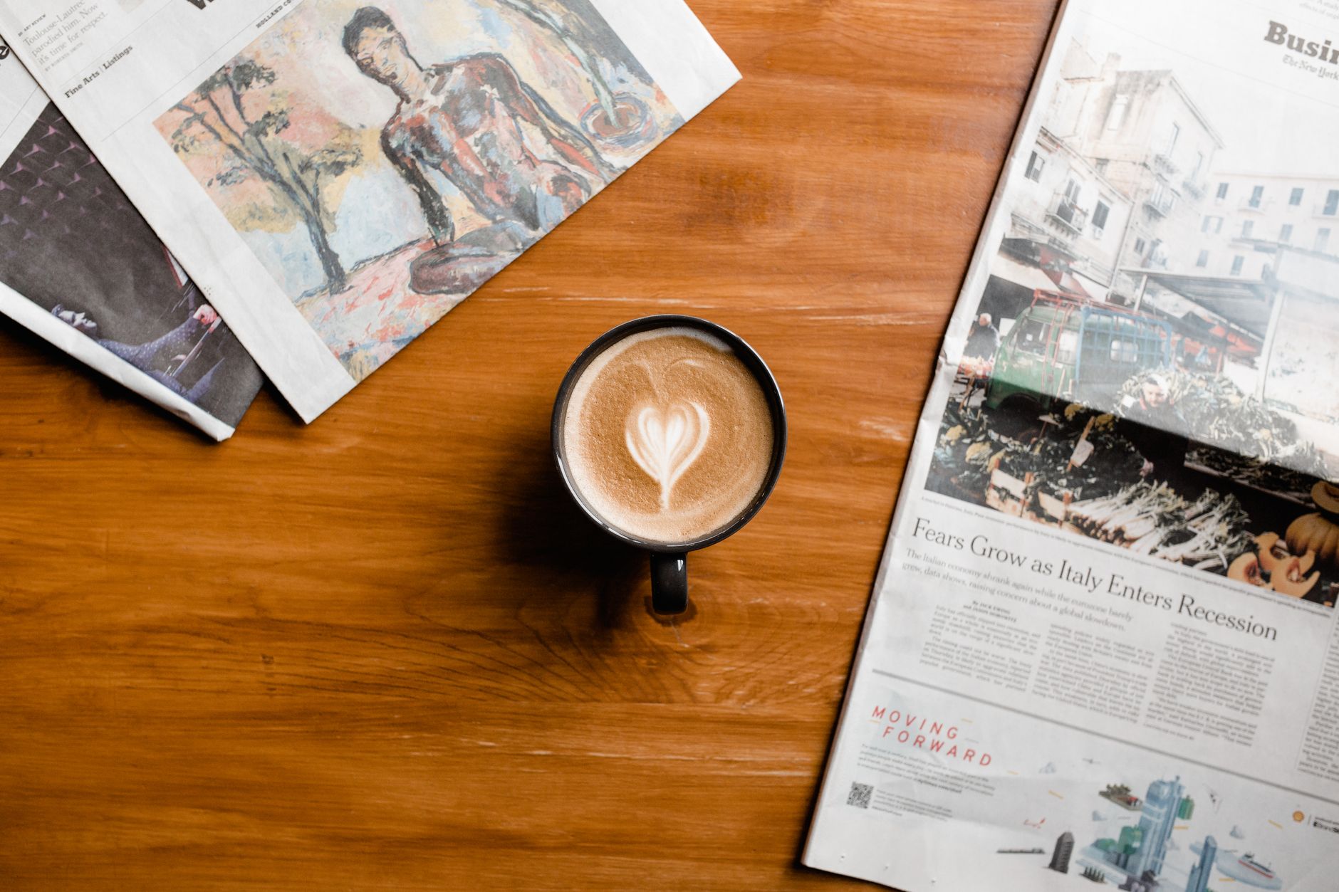 A cup of latte art on a wooden table surrounded by newspapers, perfect for cozy mornings.