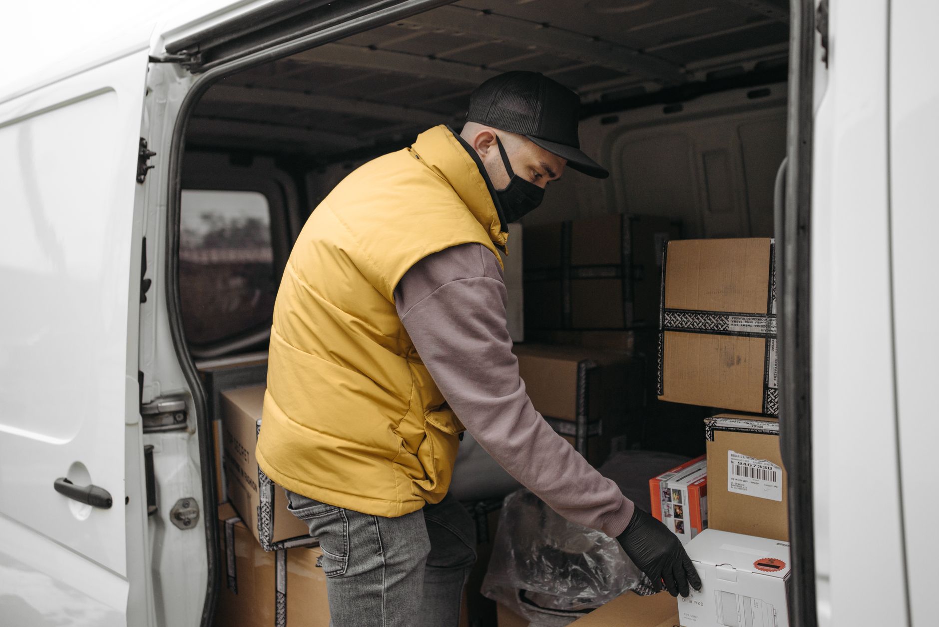 Courier organizing boxes in a van, wearing a facemask and gloves for safety.