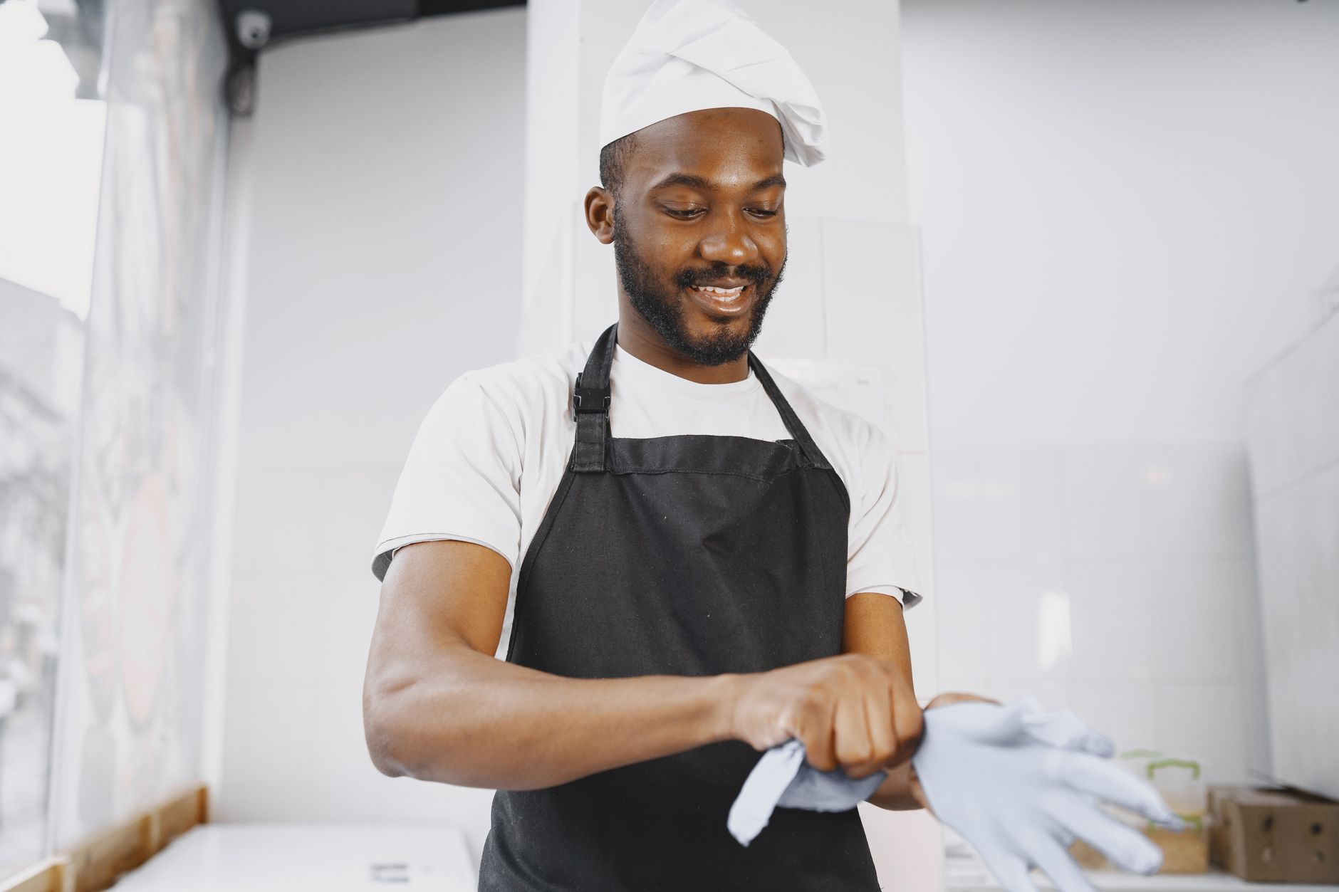 A friendly baker puts on gloves in a bakery, ready to work with joy.
