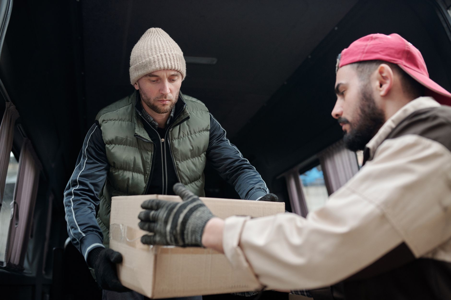 Two men unloading a cardboard box from a delivery van, showcasing teamwork.