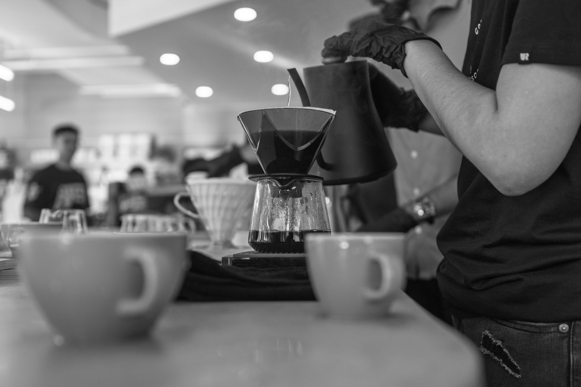 Black and white image of coffee brewing in a bustling cafe setting.