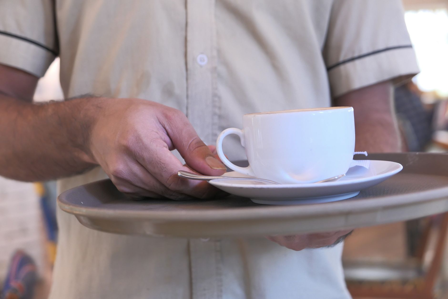 Close-up of a waiter holding a coffee cup on a tray in a café environment.