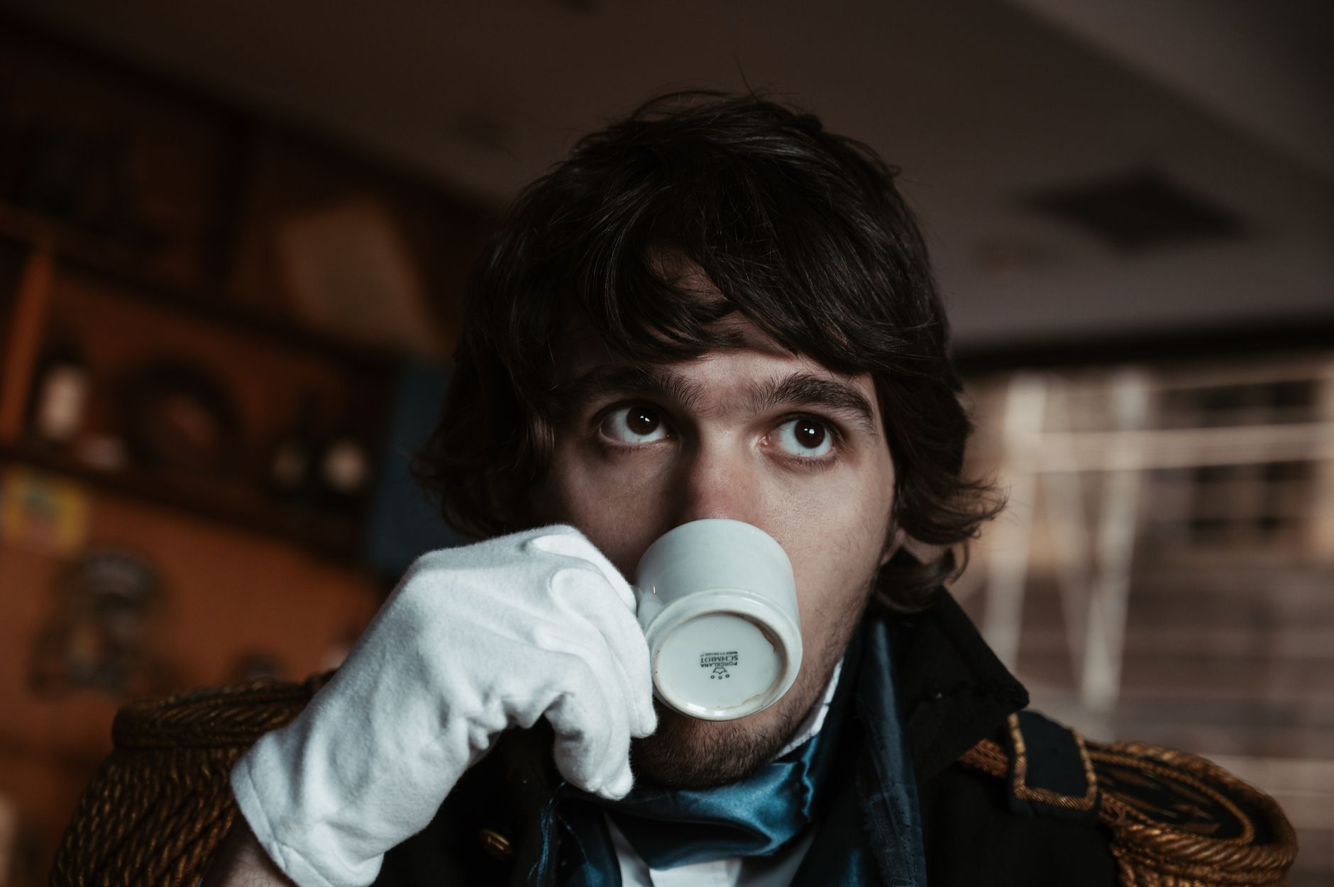 A young man dressed in historical attire enjoys an espresso indoors.