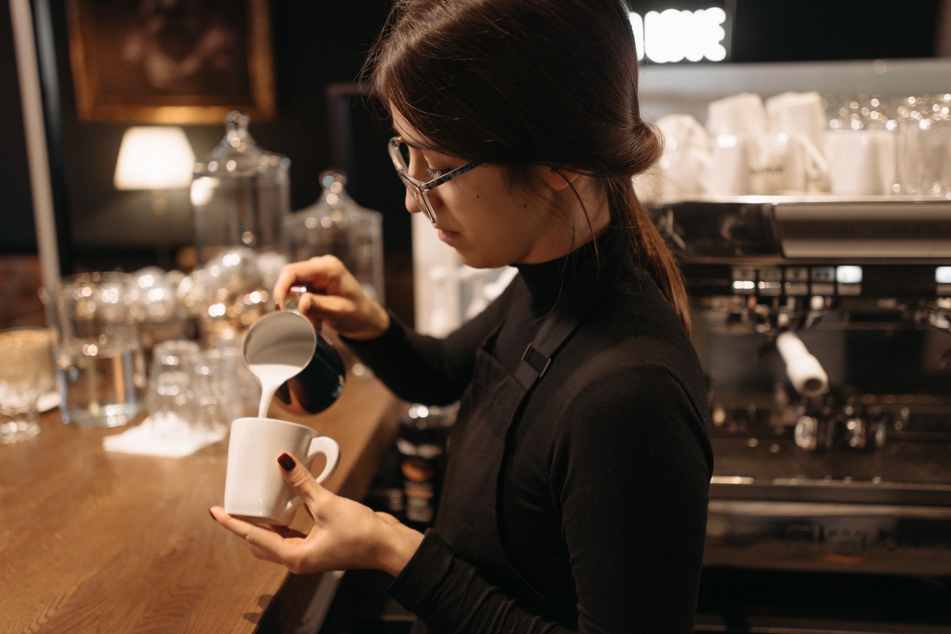 A barista expertly pours milk into coffee, creating art in a cozy coffee shop setting.