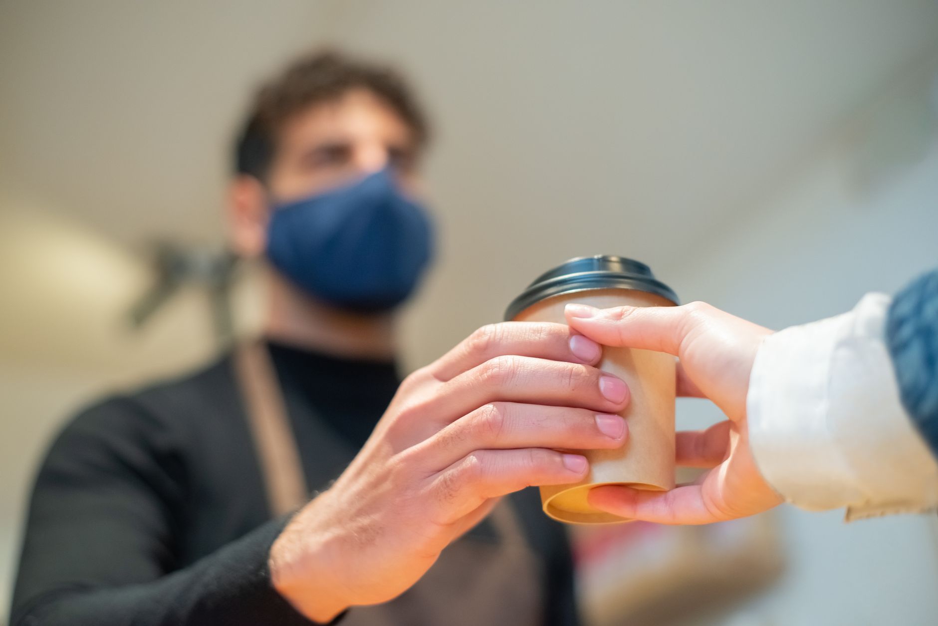 Barista hands over a to-go coffee cup with a focus on hand hygiene and service.