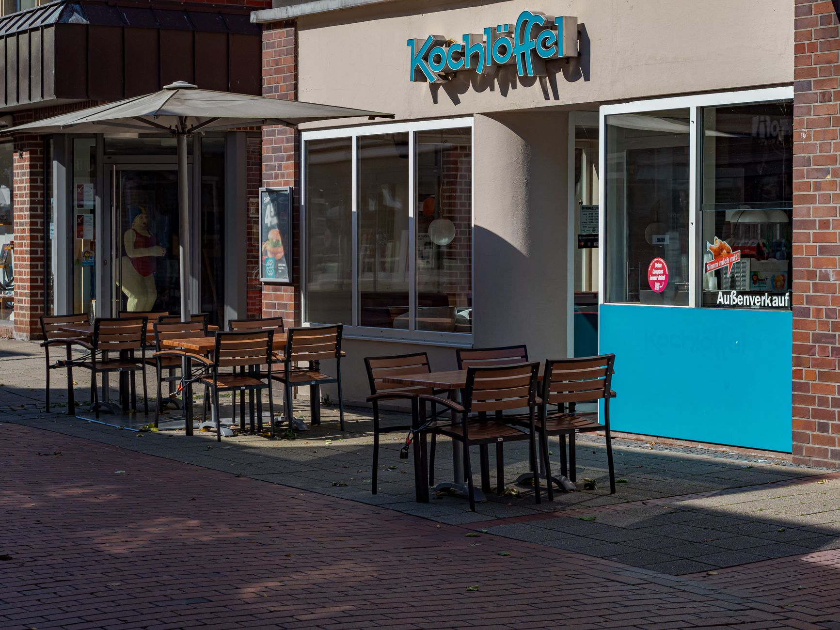 Sunny outdoor seating area of Kochlöffel restaurant in Coesfeld, Germany, with empty chairs and tables.