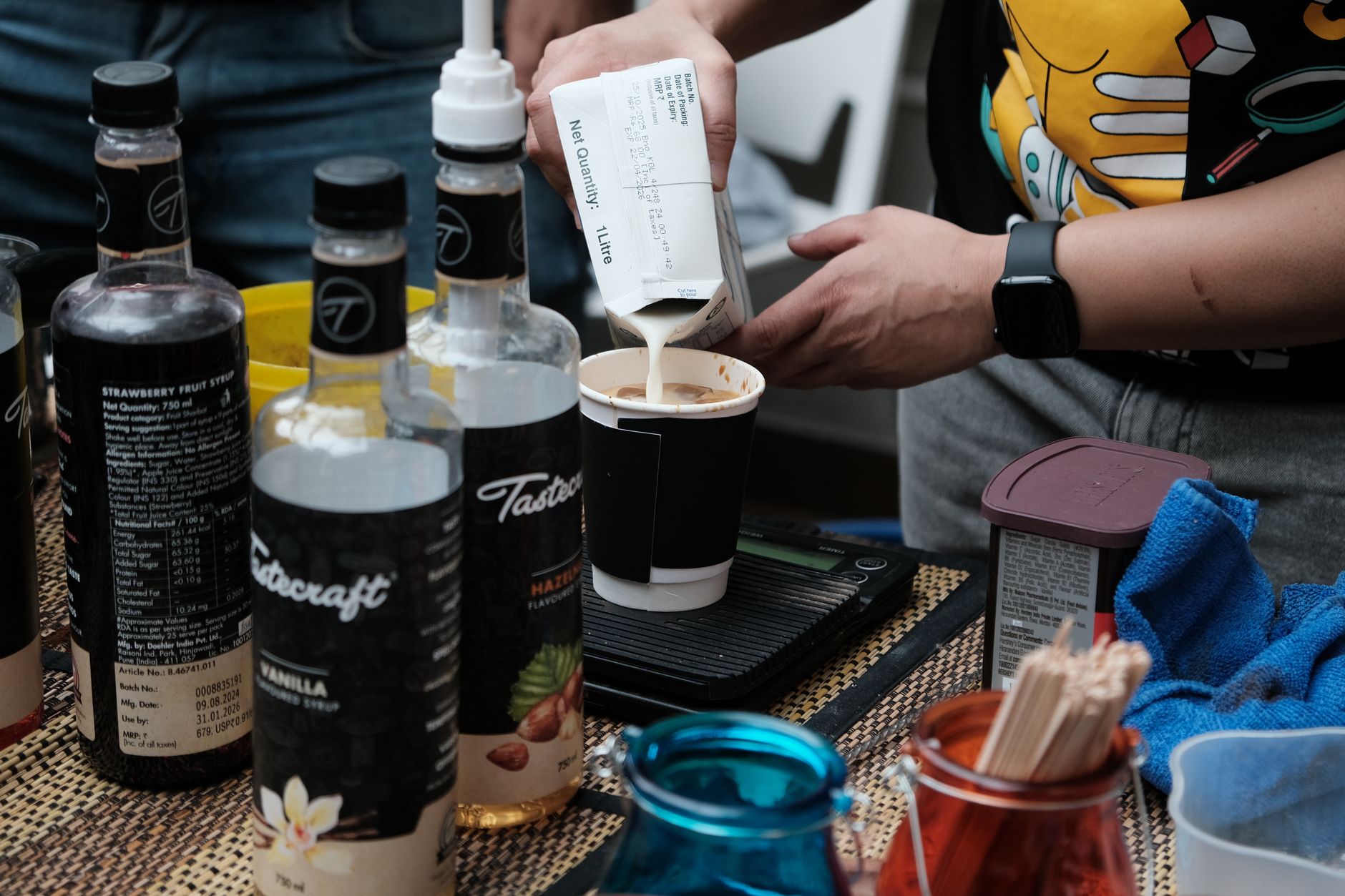 Barista making coffee with syrups and pouring milk, showcasing coffee preparation indoors.