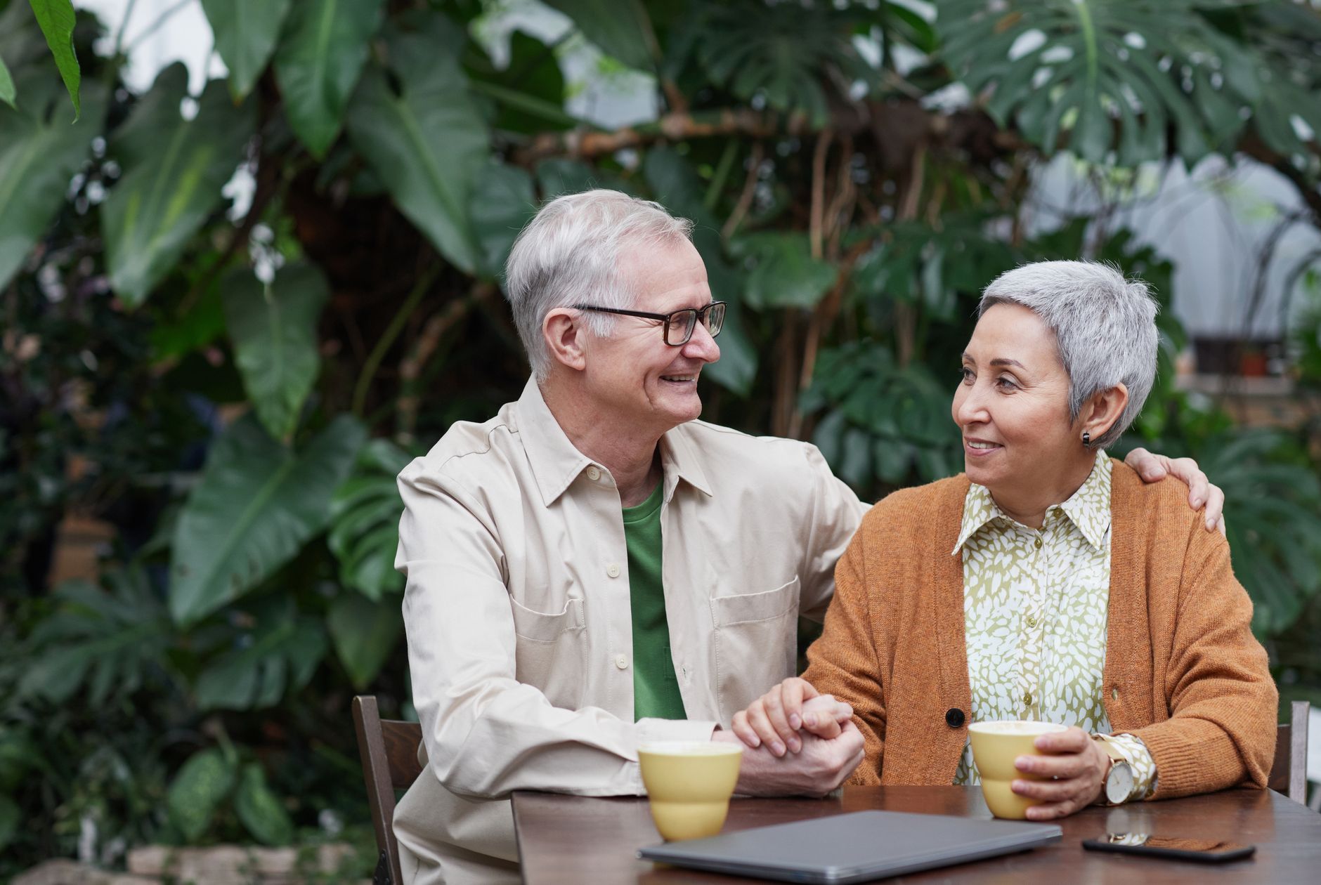 A cheerful elderly couple sharing coffee and affection at a rustic outdoor setting.