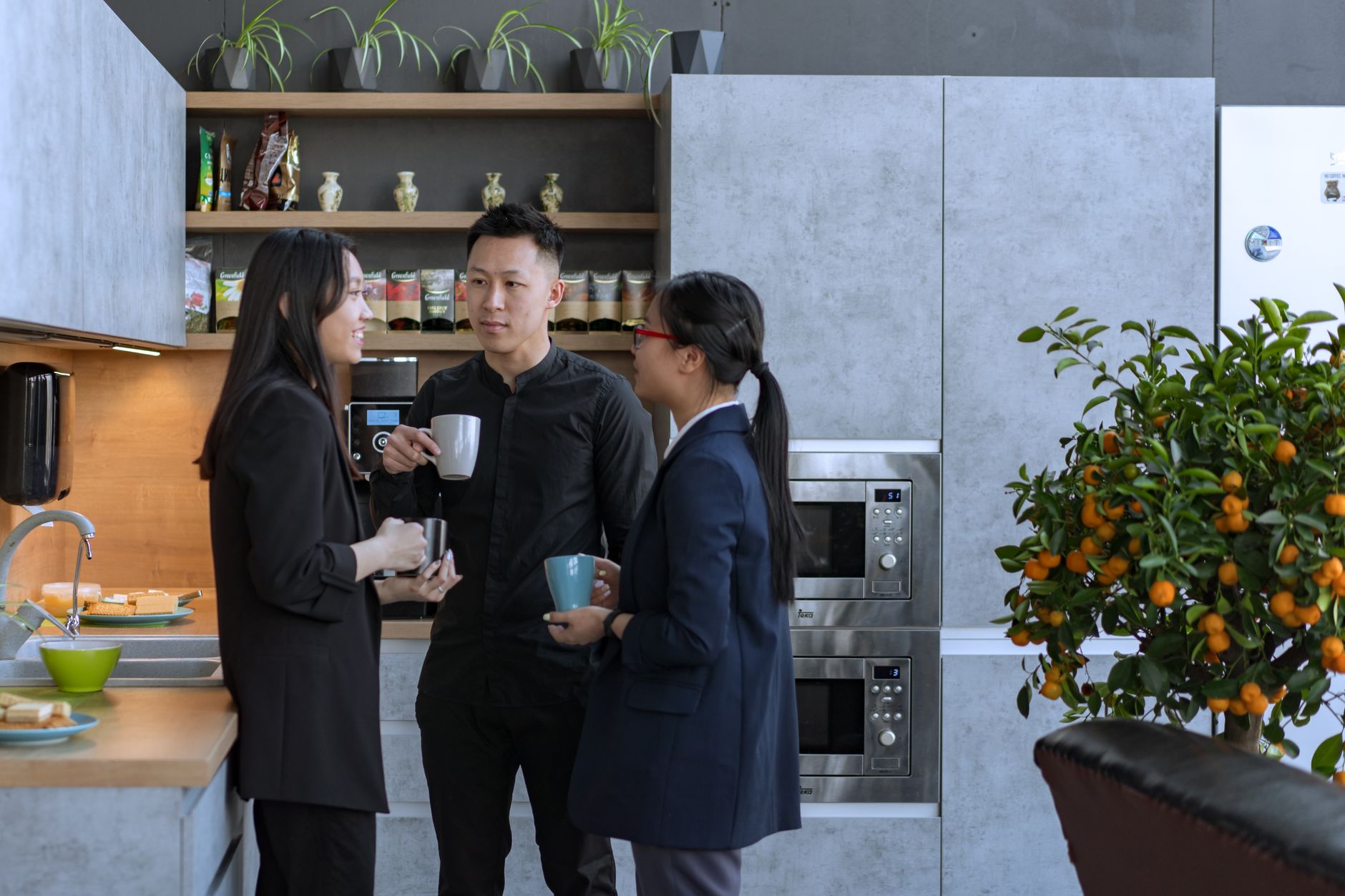 Asian professionals enjoy a coffee break and conversation in a modern office kitchen.