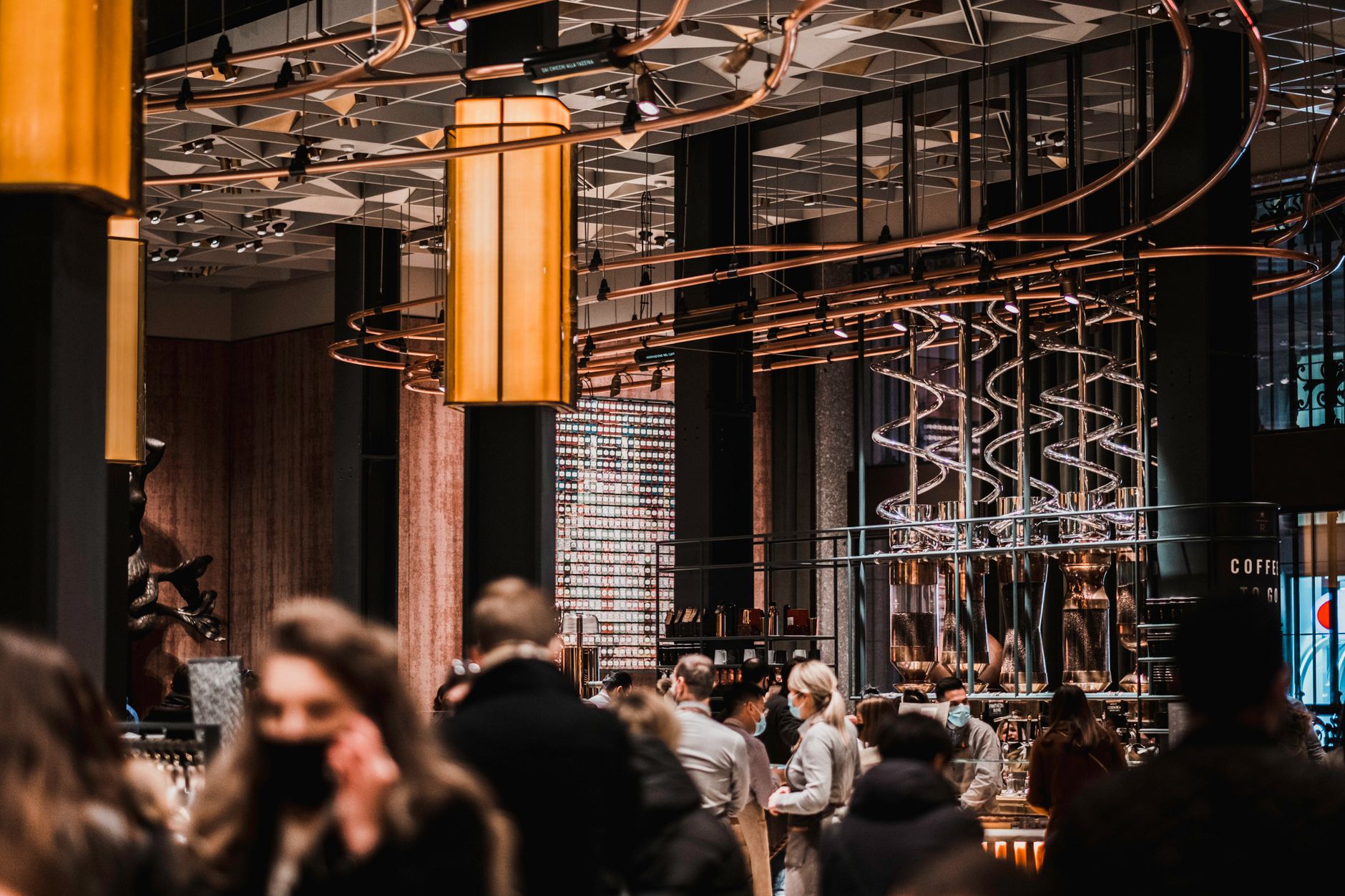 A busy coffee shop interior showcasing modern design with people wearing masks, reflecting the new normal.