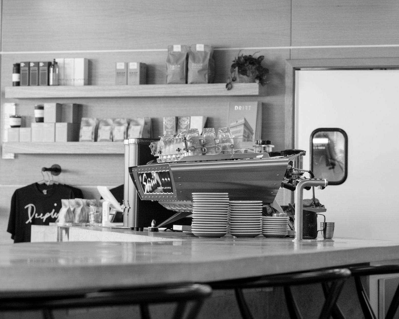 Black and white photo of a modern café with coffee machine and bar counter, showcasing elegant design.