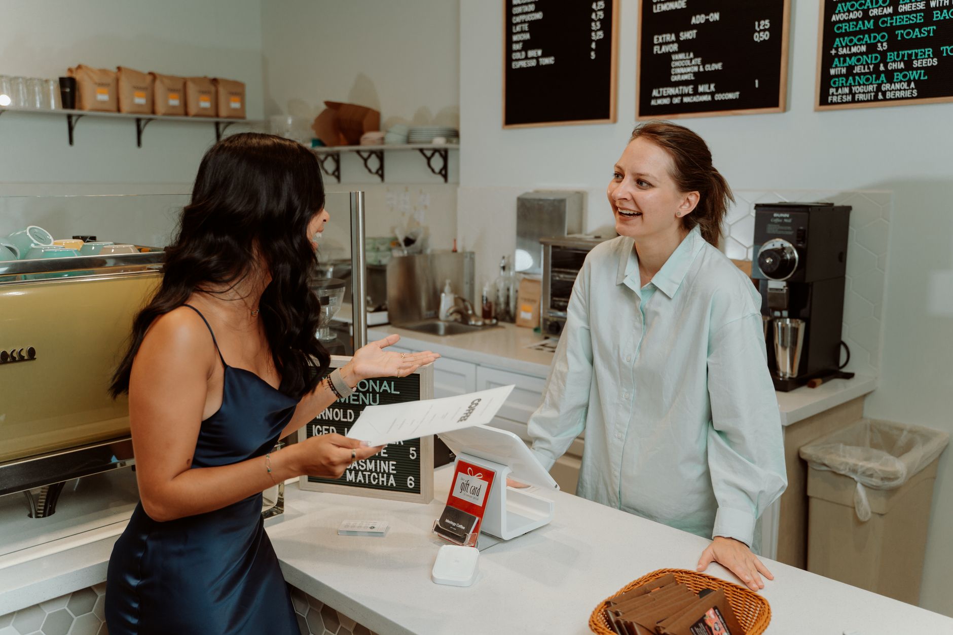 Two women engaging in a cheerful conversation at a modern café counter.