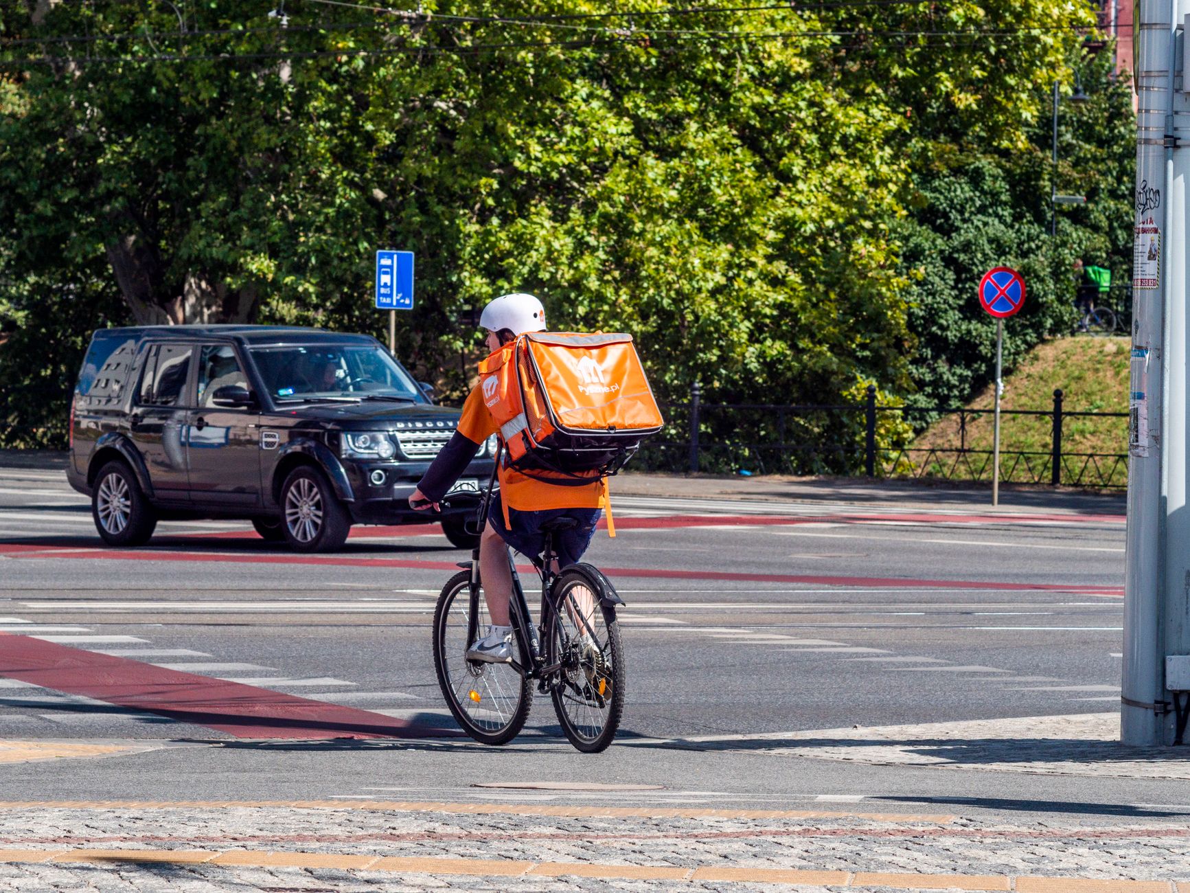 Bicycle courier with insulated backpack crossing city street on a sunny day.