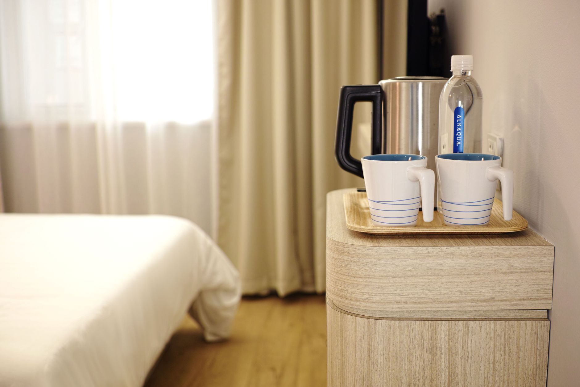 Contemporary hotel room featuring a neatly arranged beverage setup on wooden furniture.