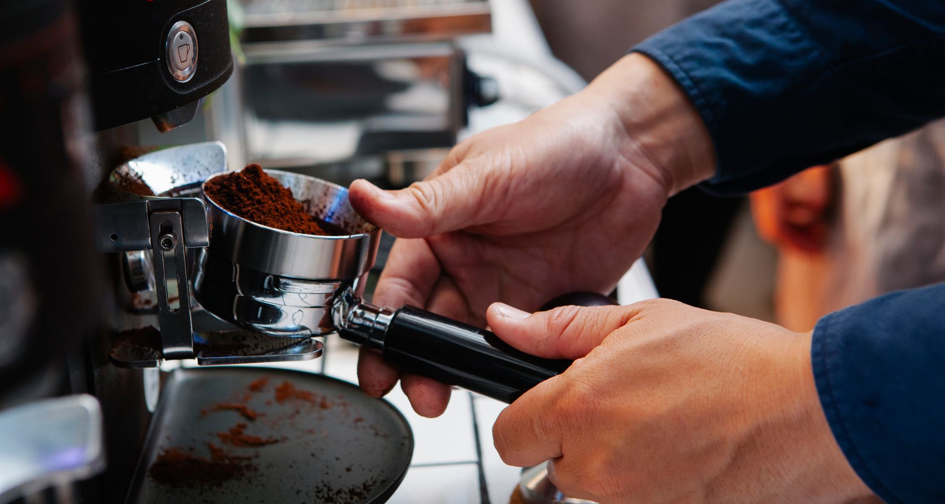 Crop unrecognizable male cafe employee inserting metal portafilter with ground coffee into electric maker in kitchen