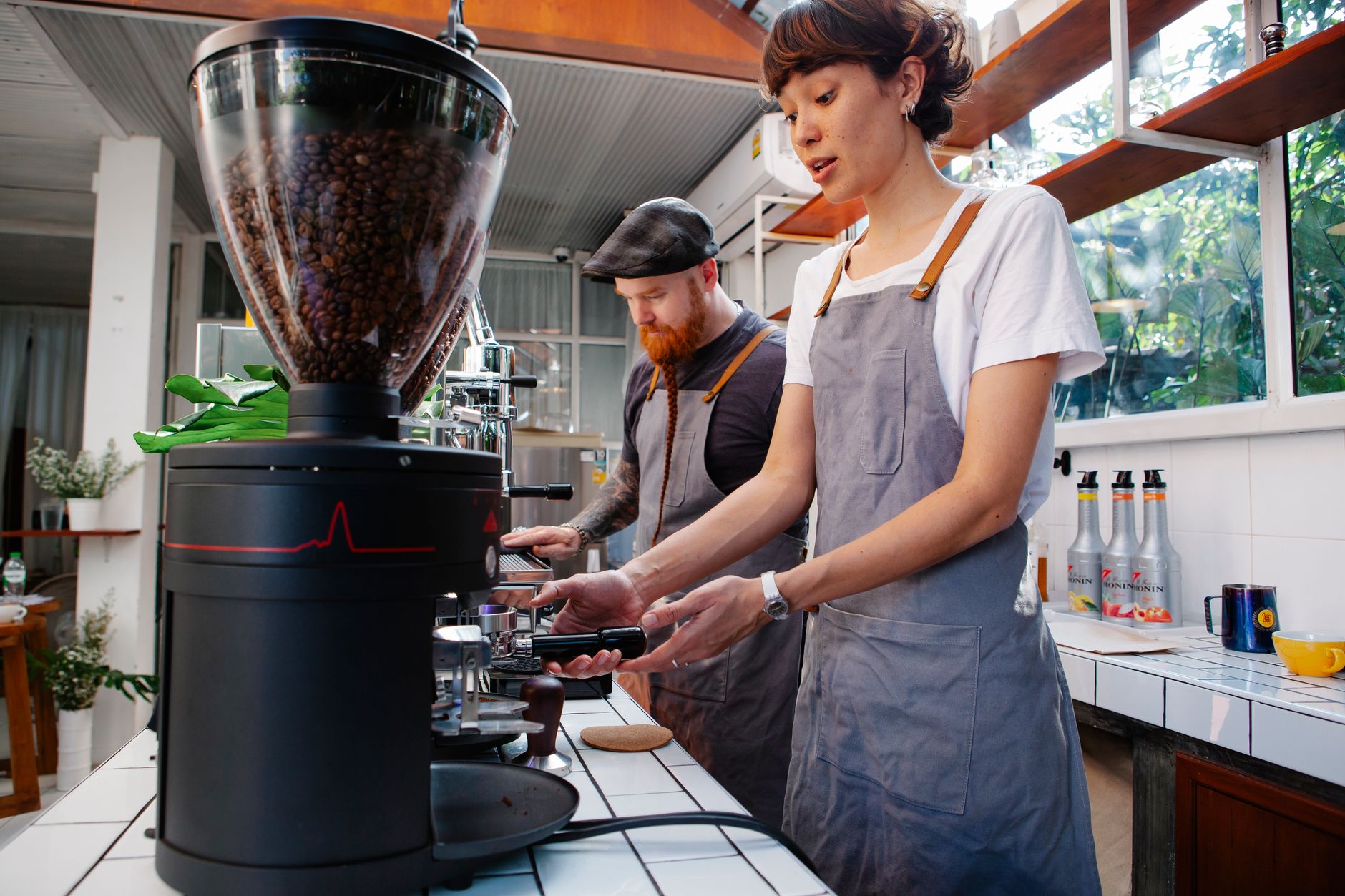 Crop young female employee with hipster male partner preparing hot drinks in professional coffee machines in cafeteria