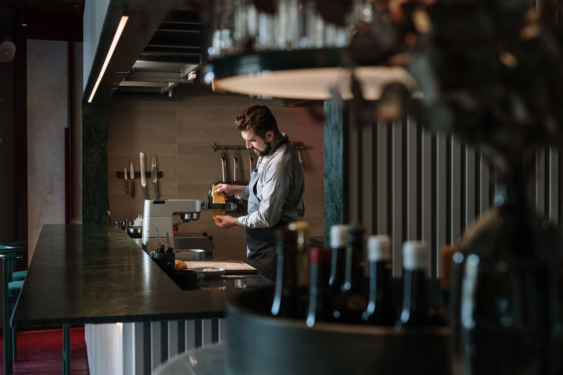 A male chef meticulously prepares a dish in a contemporary restaurant kitchen, surrounded by culinary tools.