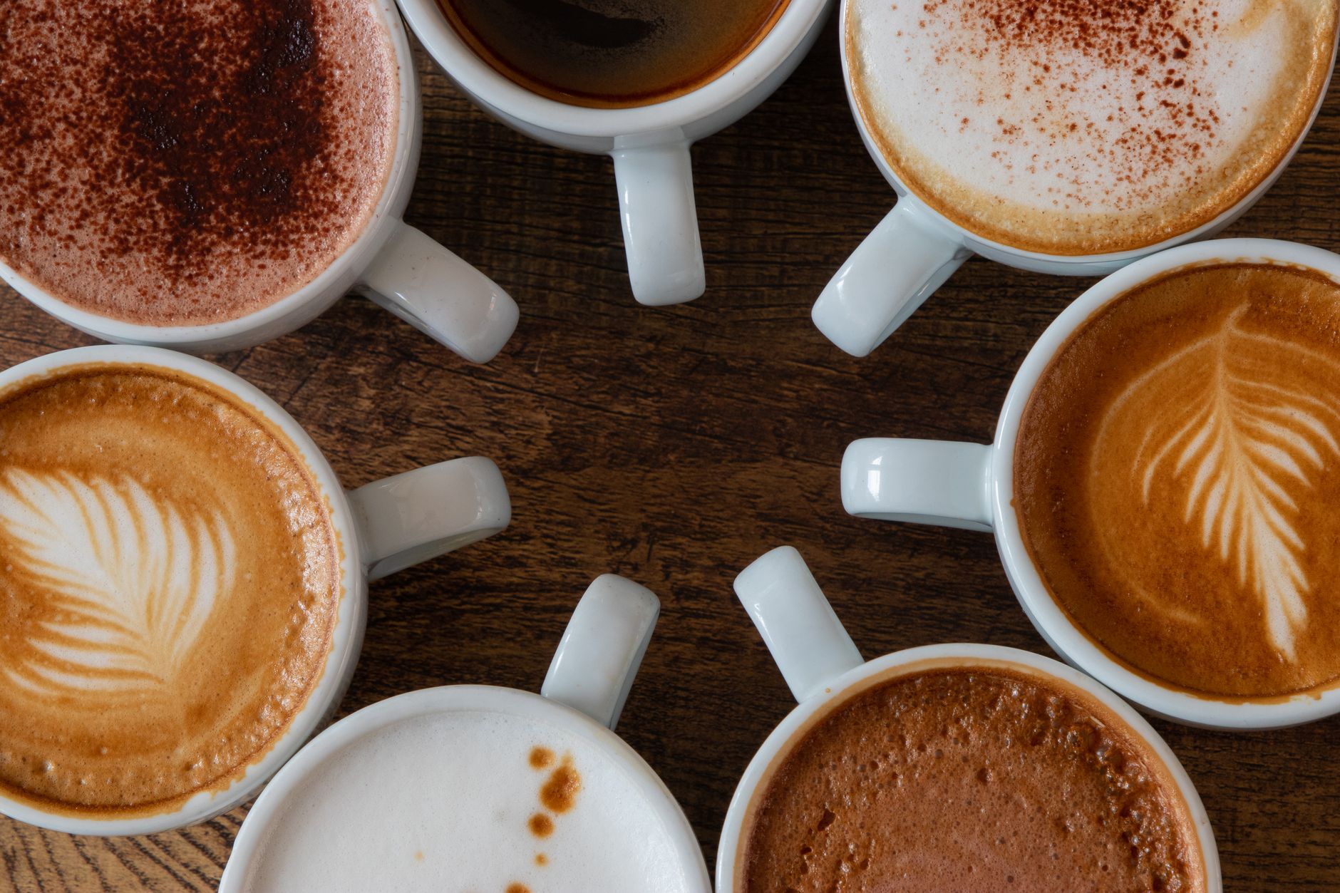 A circle of coffee cups showcasing various latte art designs from a top view.