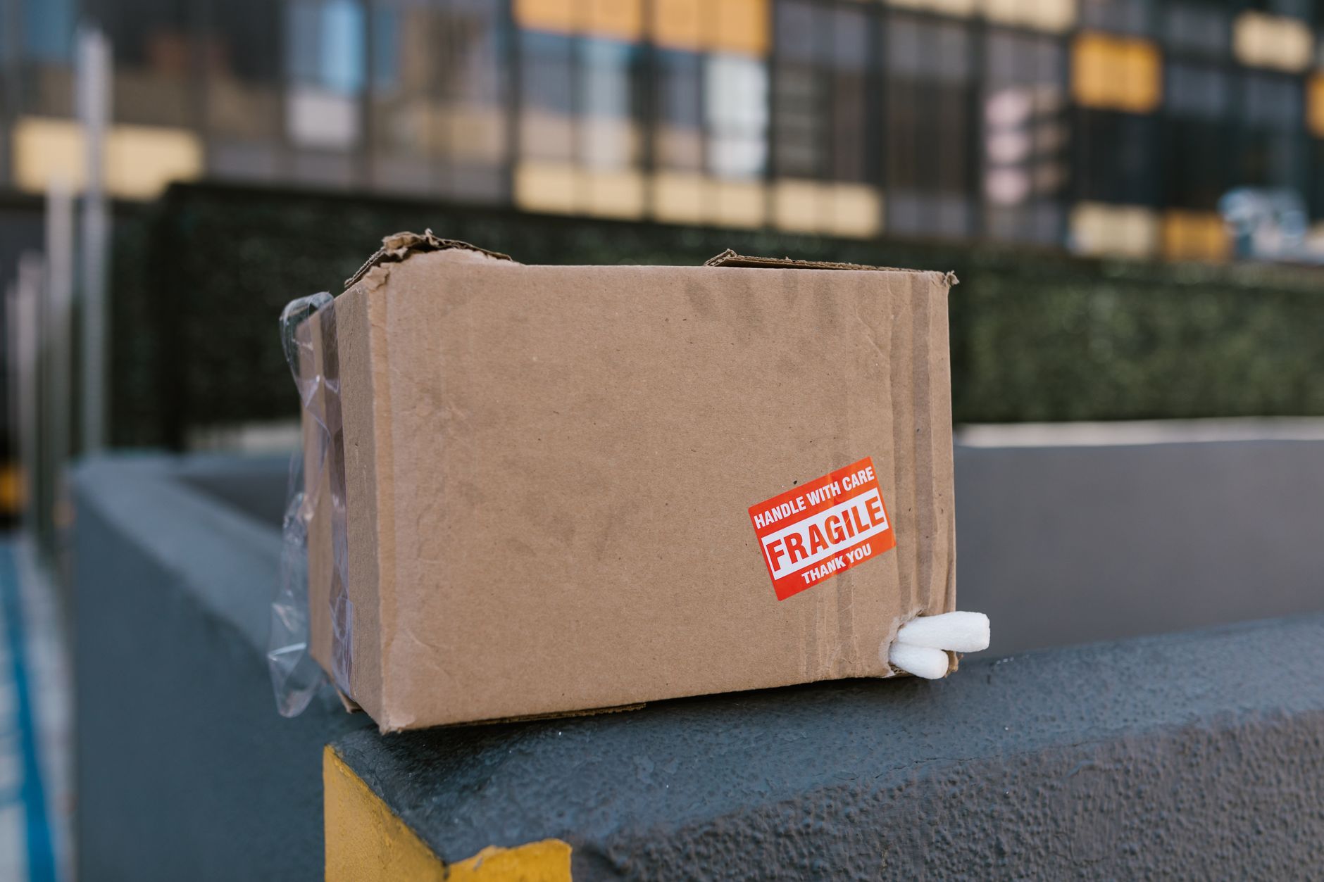 Close-up of a fragile cardboard box on a concrete ledge in an urban setting, symbolizing delivery challenges.