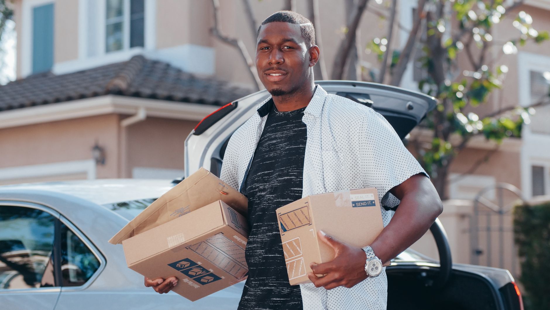 A courier in a residential area delivering packages from a car trunk, representing efficient delivery service.