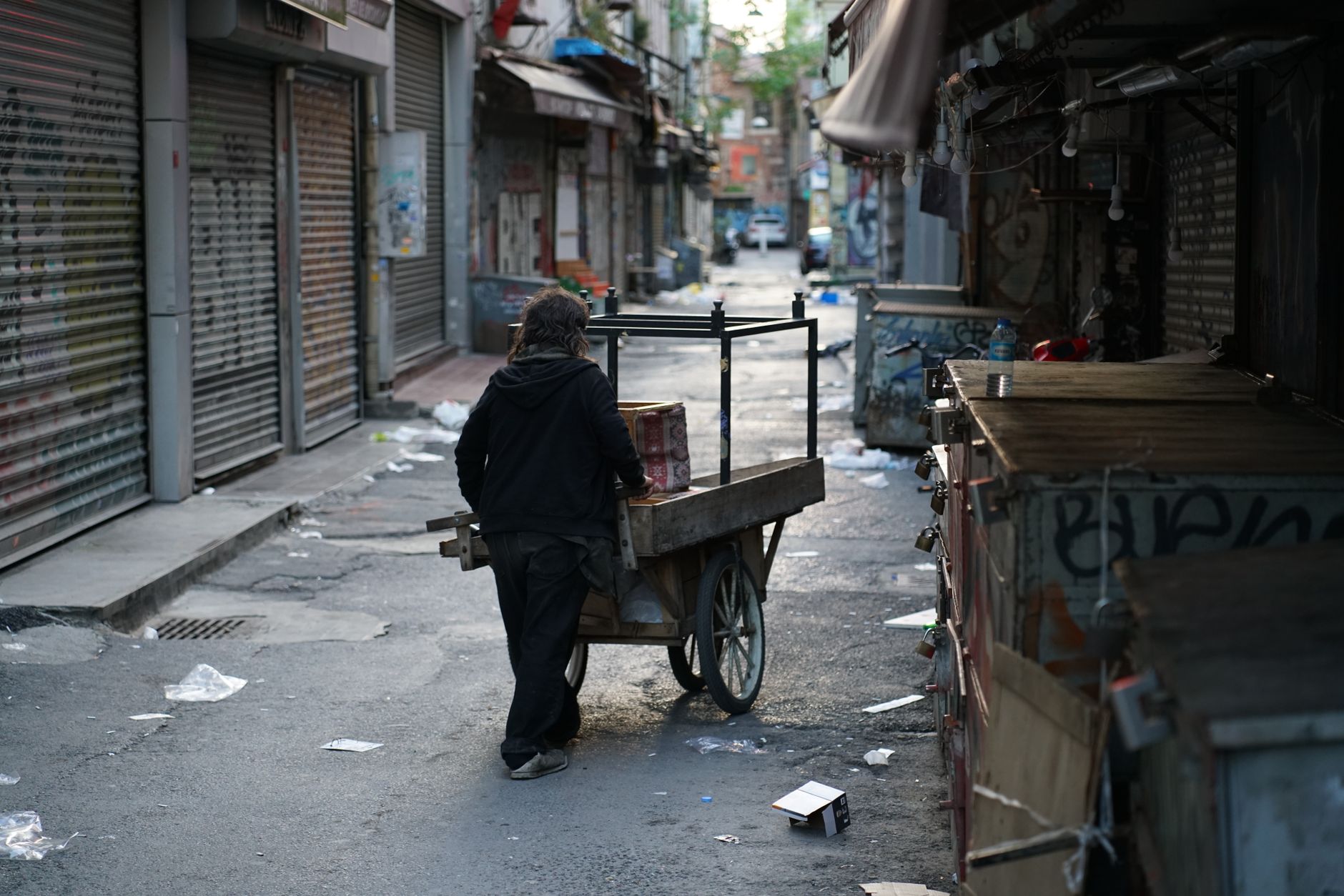 A solitary person pushes a cart through a graffiti-covered urban alleyway.