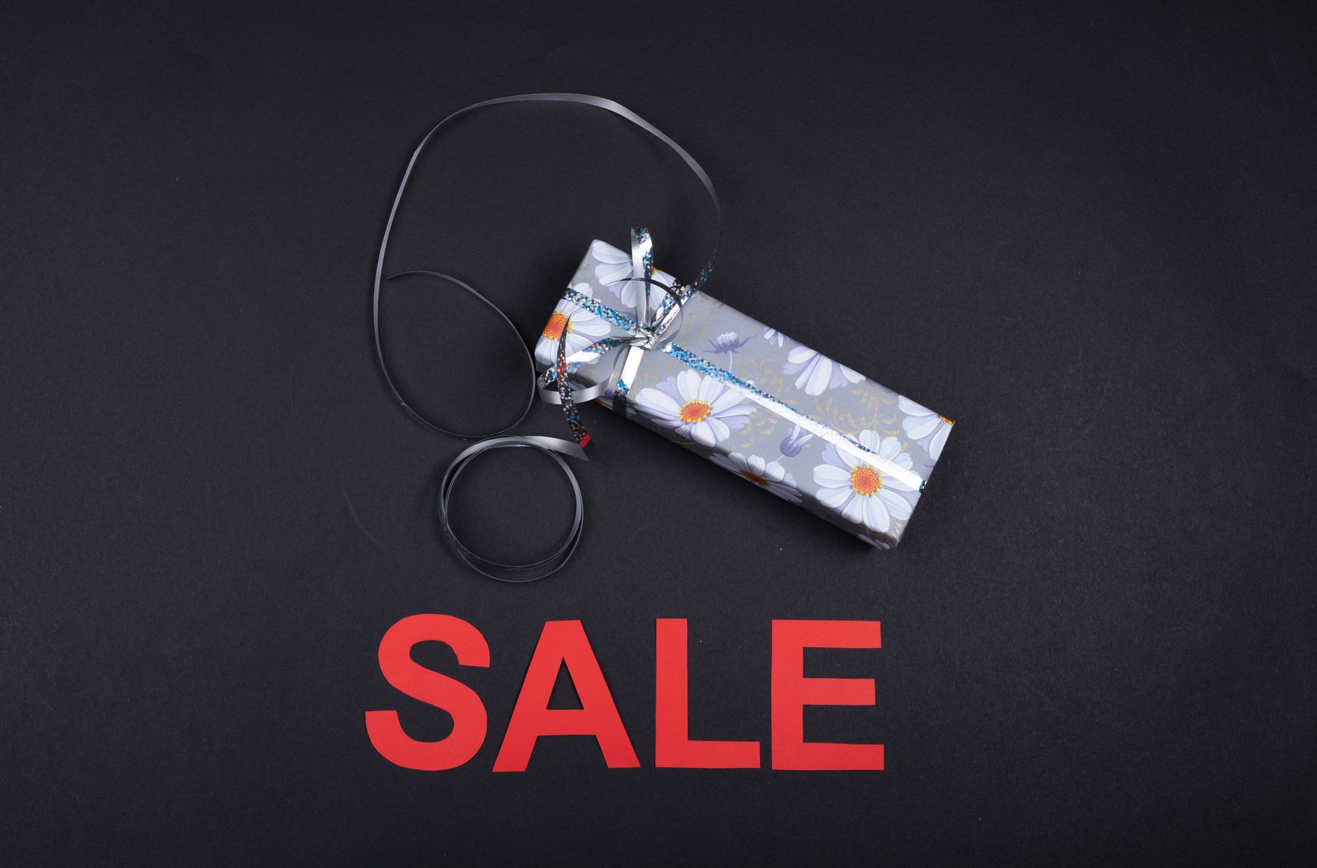 Floral wrapped gift box with ribbon on black background, featuring bold sale text in red.