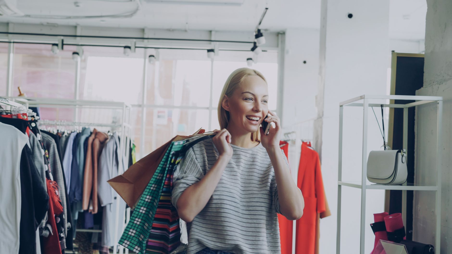 Smiling woman carries shopping bags and talks on the phone in a clothing store.