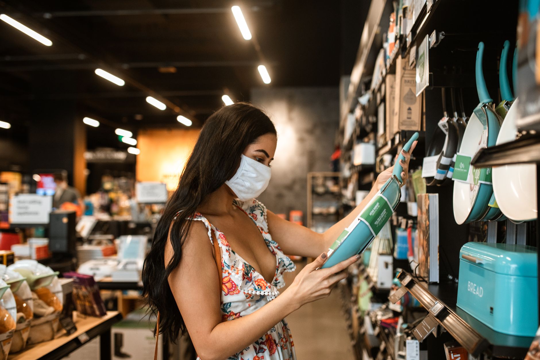 Stylish woman with mask shopping for cookware in a modern store.