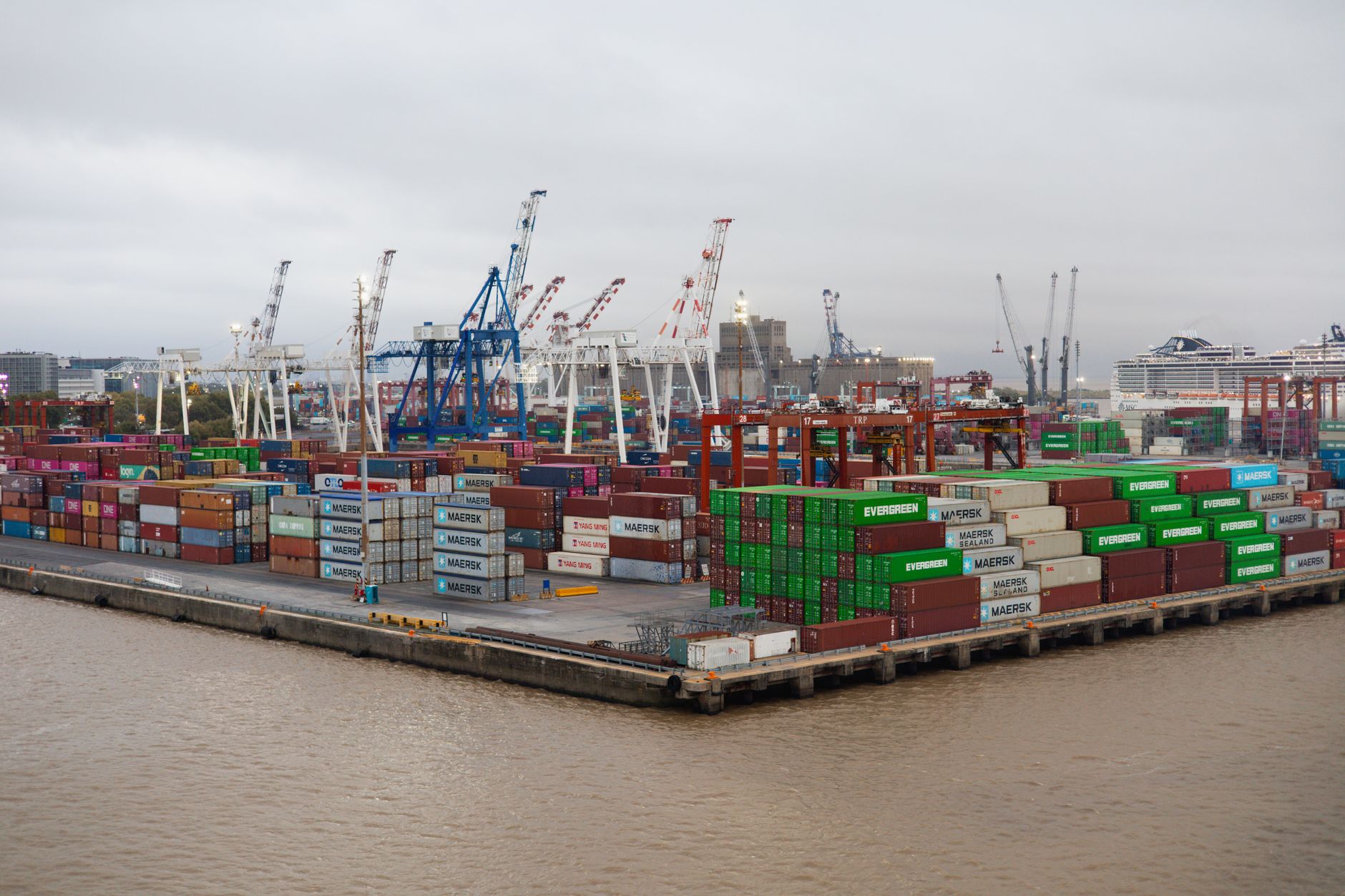A bustling shipping port with stacked cargo containers and cranes under overcast skies.