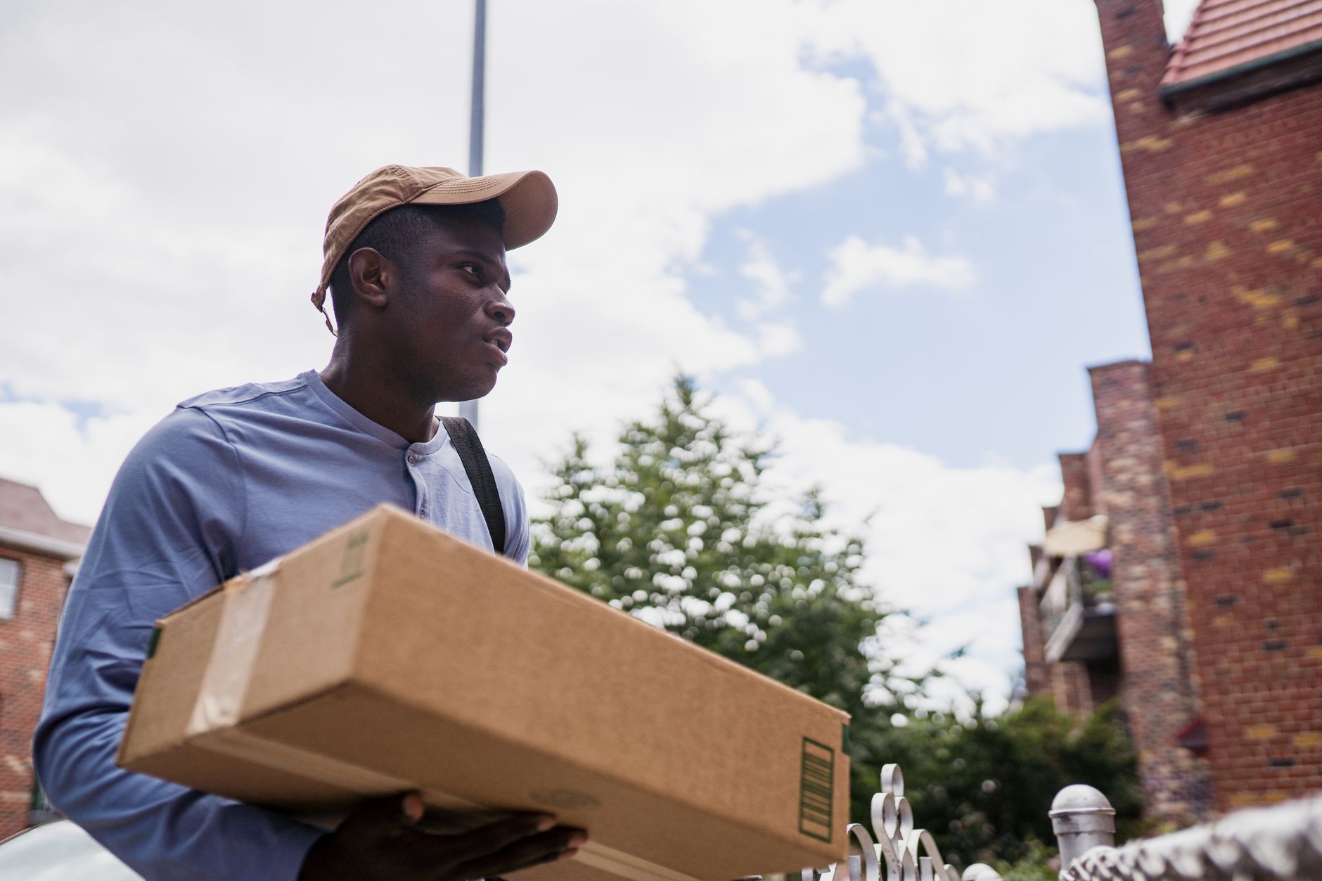 A man carrying a cardboard box outdoors in a residential area.