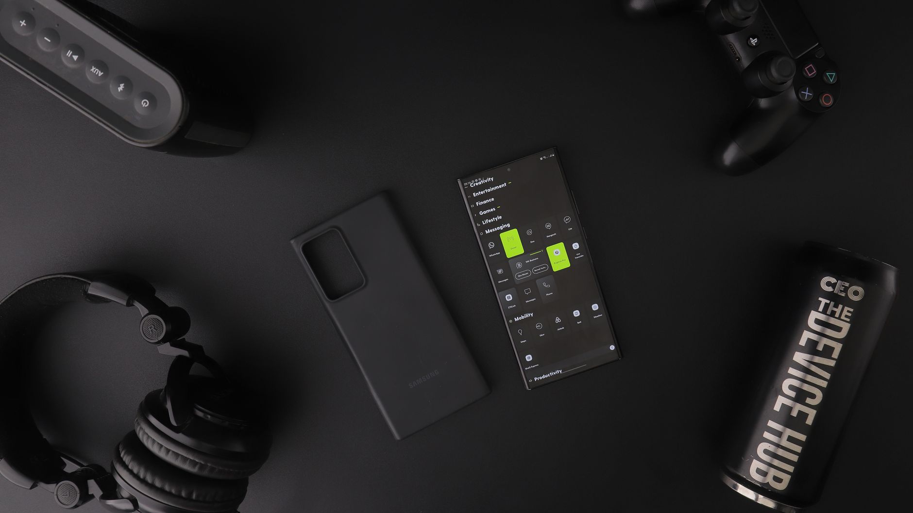 Overhead view of black modern electronics including smartphone, headphones, speaker, and controller on a table.