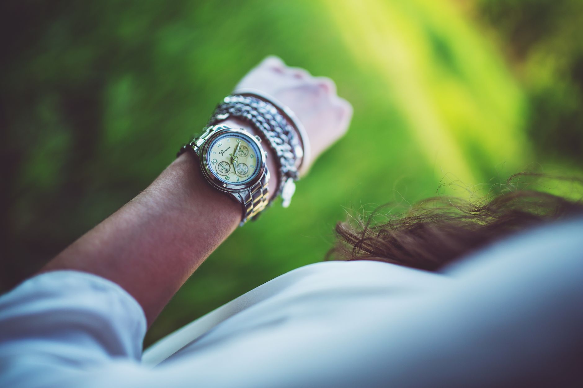 Close-up of a woman's arm wearing a silver watch and bracelets with a green background.