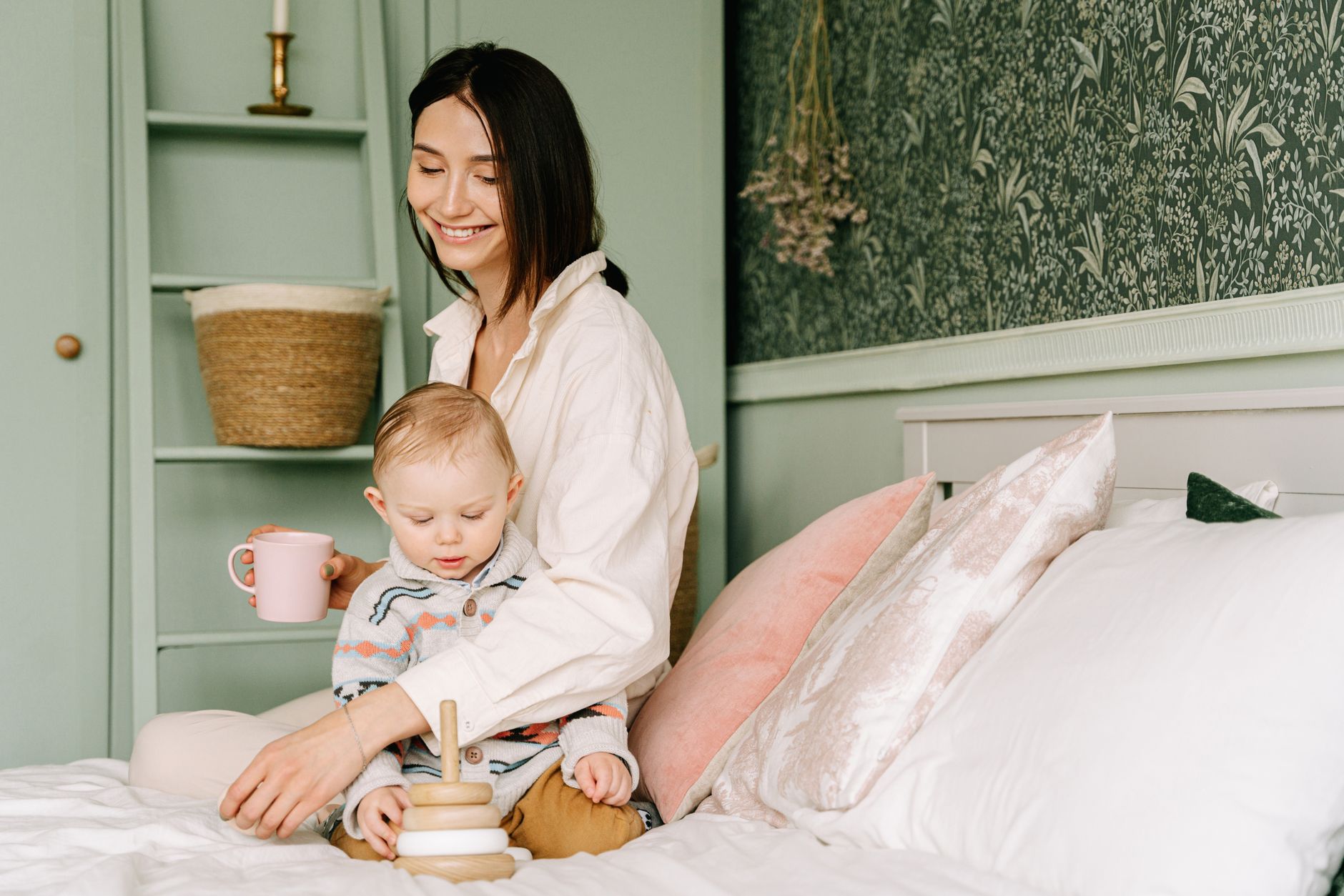 A mother enjoys quality time with her baby, playing with wooden toys on a bed in a cozy, decorated room.