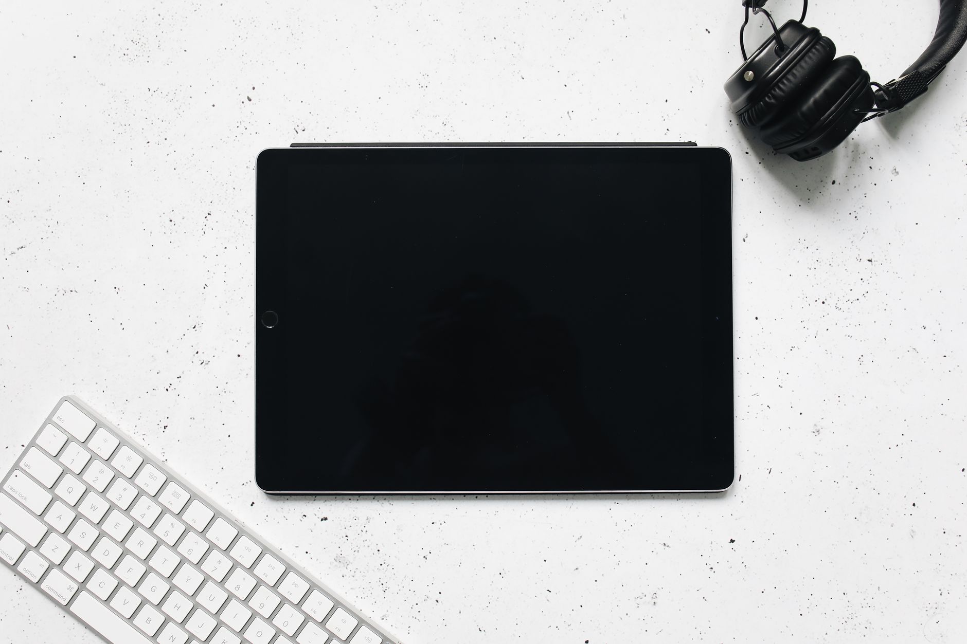 Flat lay of a digital tablet, headphones, and keyboard on a white background.