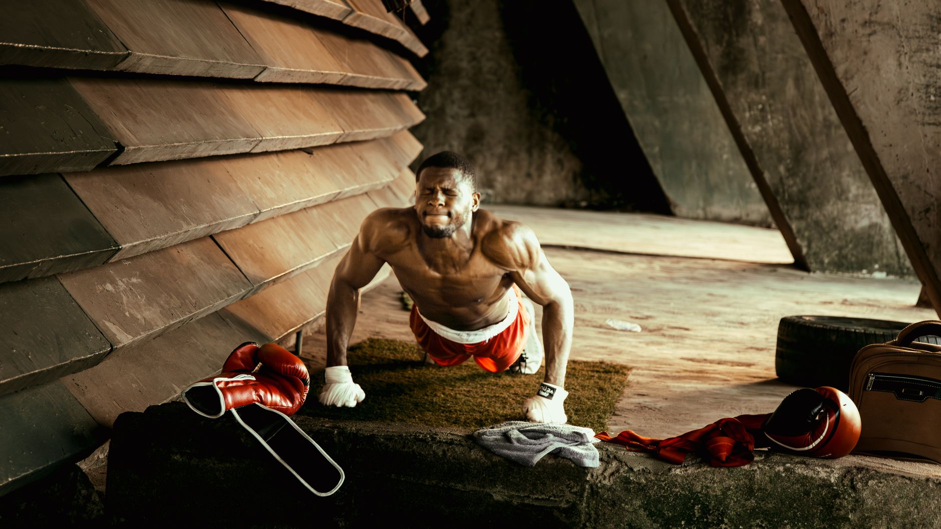 African male boxer doing push-ups in an industrial-style gym setting, showcasing strength and determination.