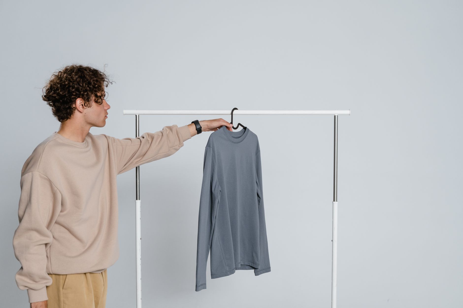 Teenage boy in casual wear holding a gray t-shirt on a rack indoors.