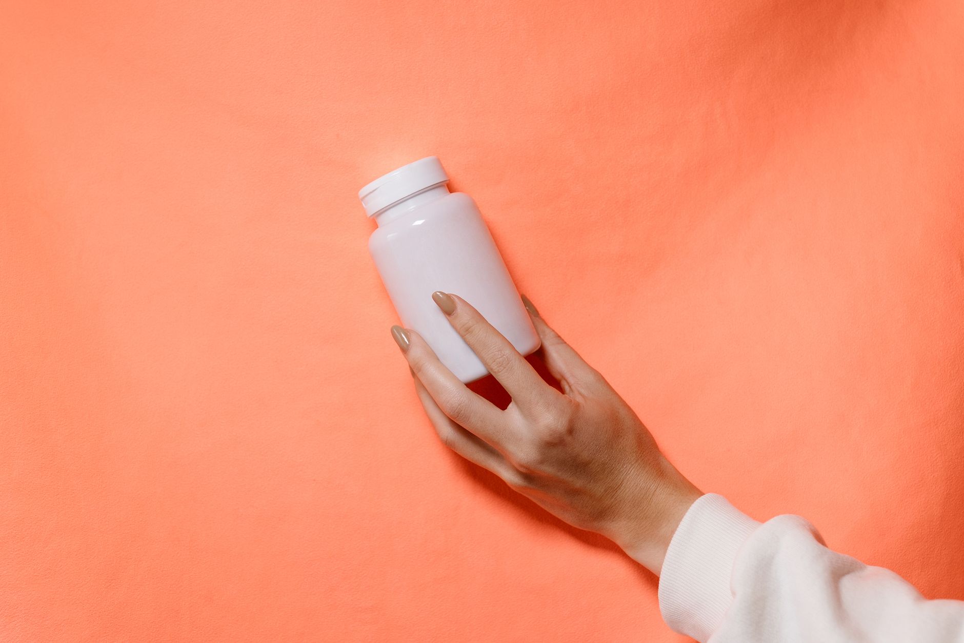 Close-up of a hand holding a white bottle against a vibrant orange backdrop.